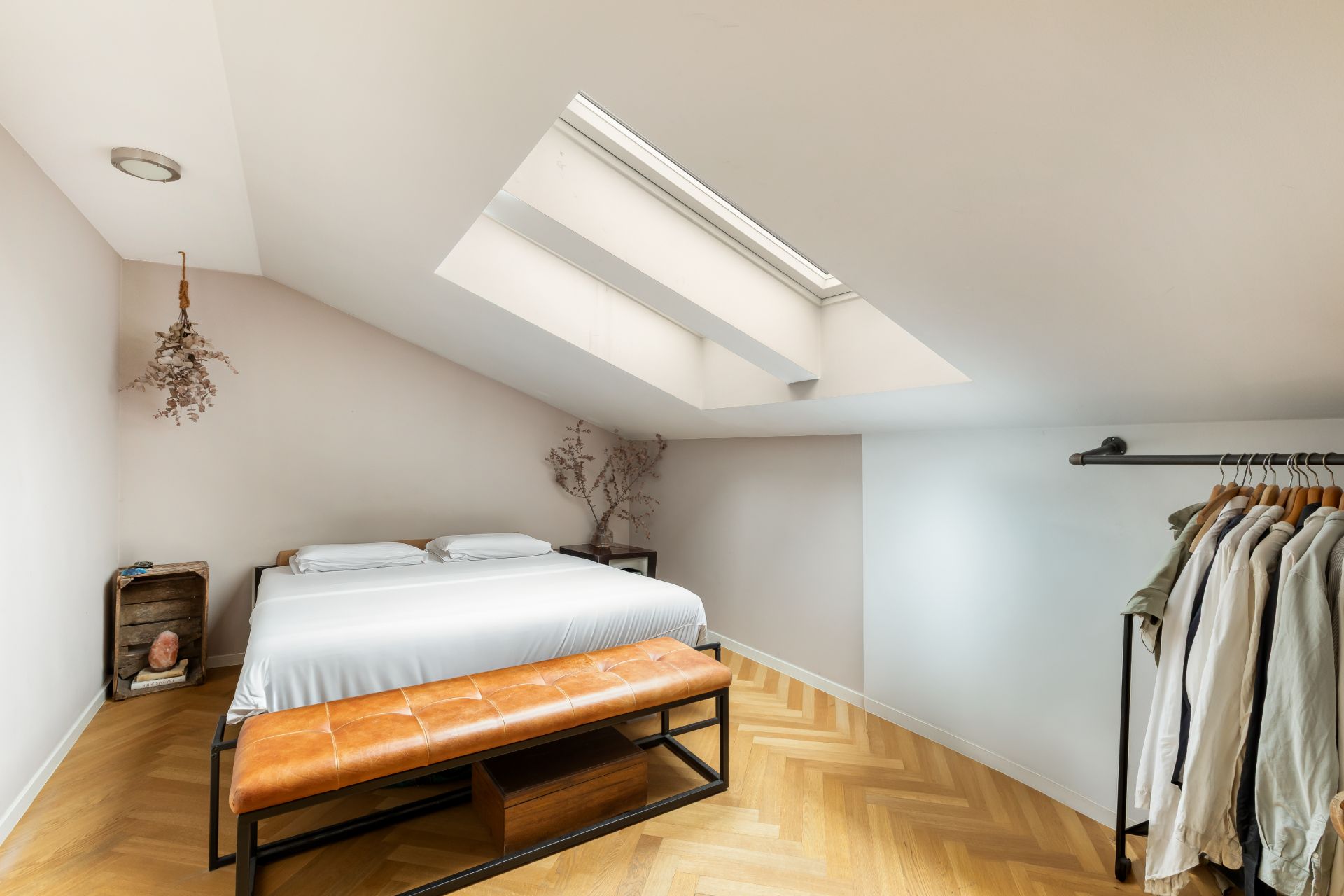 Schlafzimmer mit großem Dachfenster, Bett, Lederbank und offener Kleiderstange.