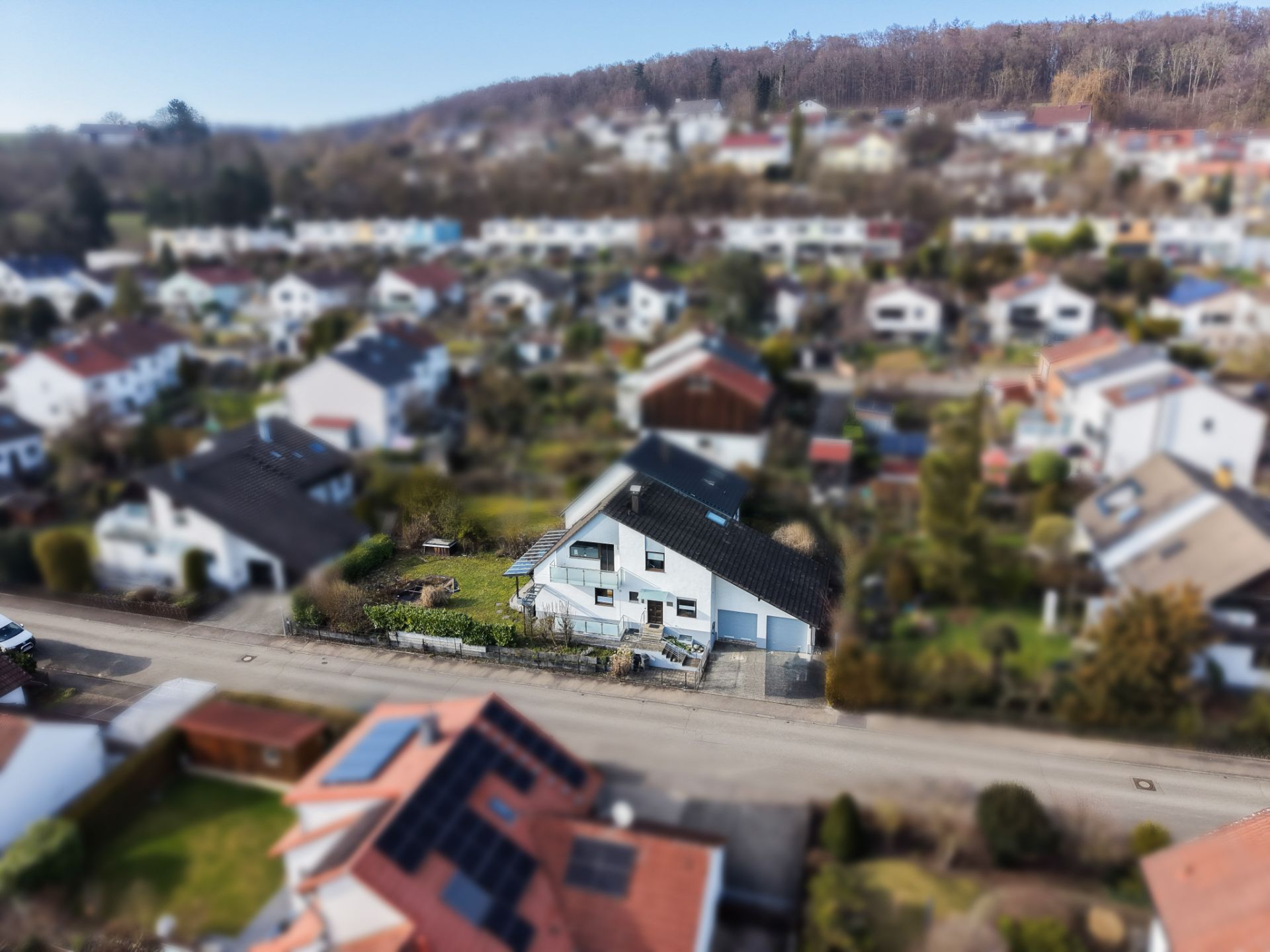 Luftaufnahme eines Einfamilienhauses in einer Wohnsiedlung mit Gärten und Straßen.