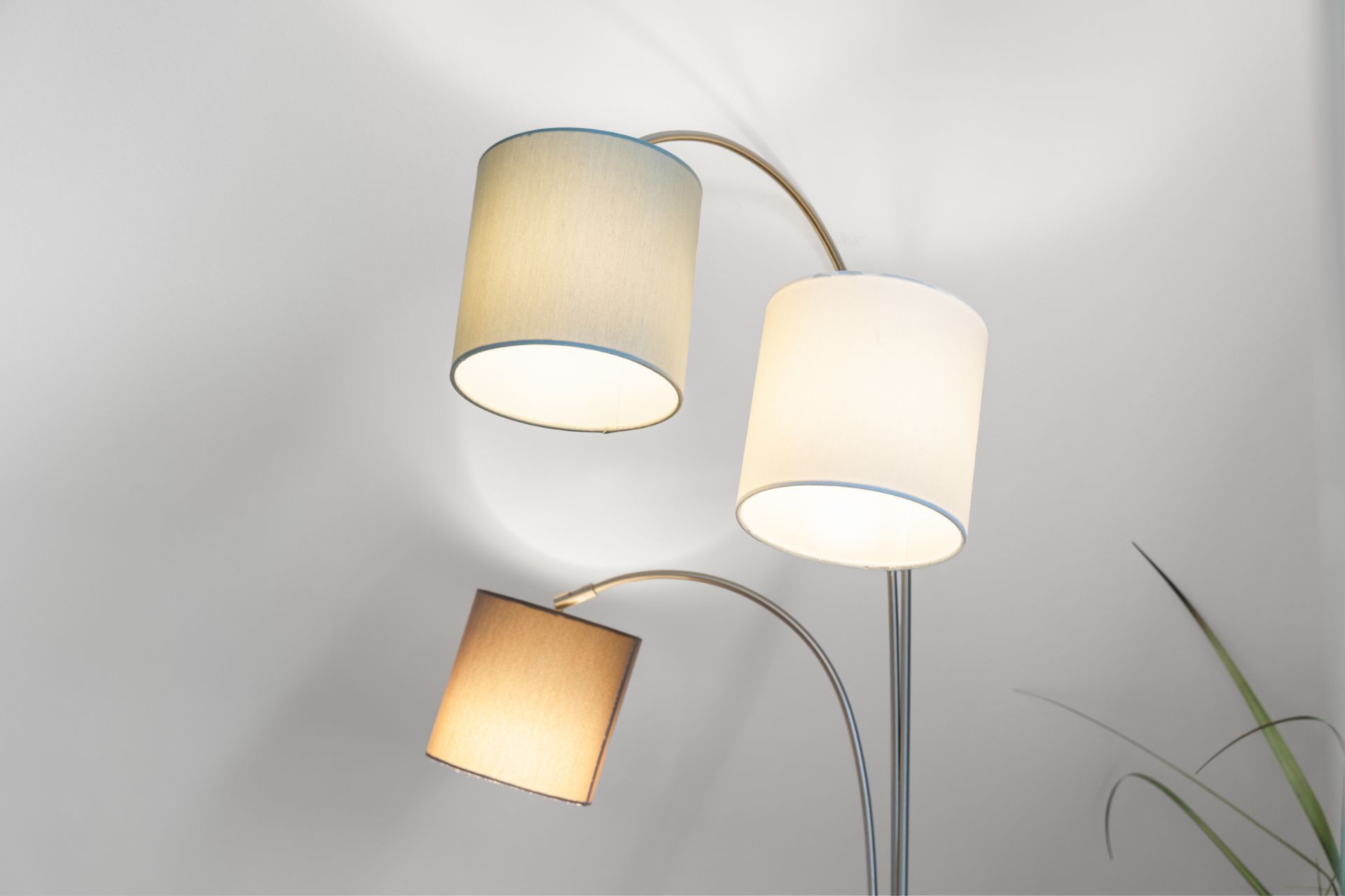 Dreifache Stehlampe mit runden, hellen Lampenschirmen vor weißer Wand.