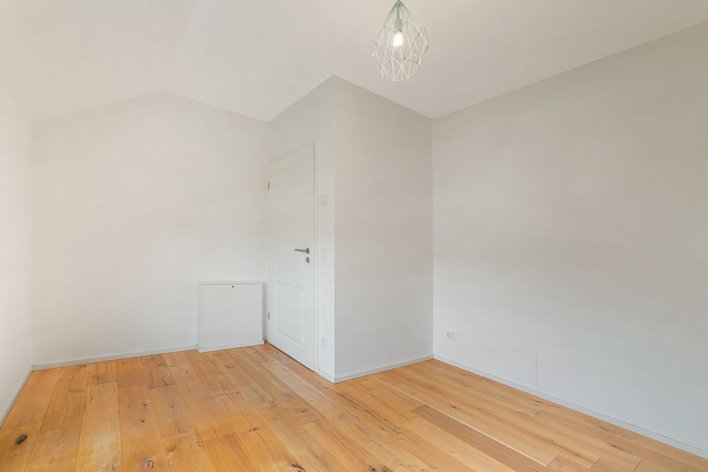 Leerer Raum mit Holzboden, weißen Wänden, Tür und Deckenleuchte.