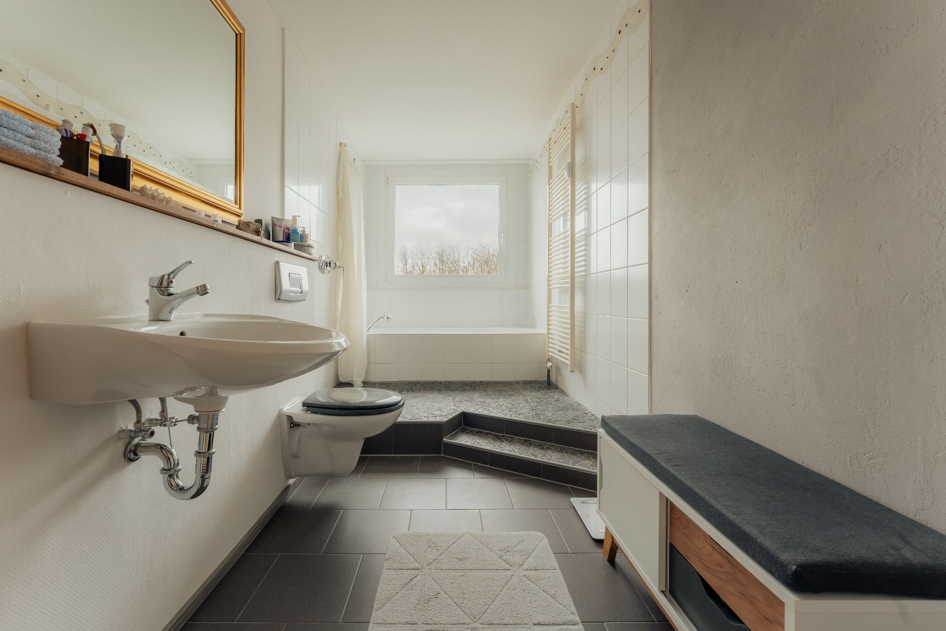 Helles Badezimmer mit Waschbecken, Toilette, Badewanne und Fenster.
