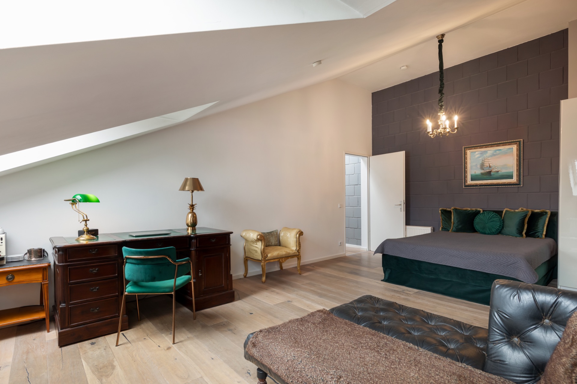 Geräumiges Schlafzimmer mit Schreibtisch, Bett, Sessel und Dachfenster.