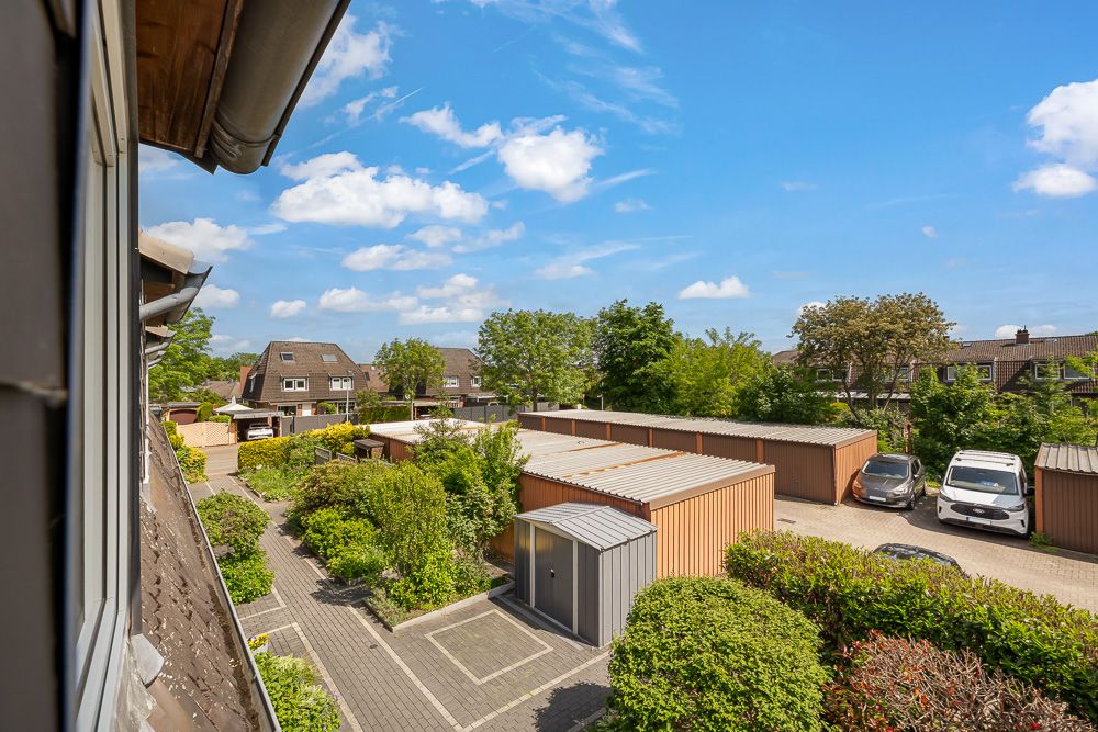 Blick aus einem Fenster auf Garagen, Grünflächen und geparkte Autos bei sonnigem Wetter.