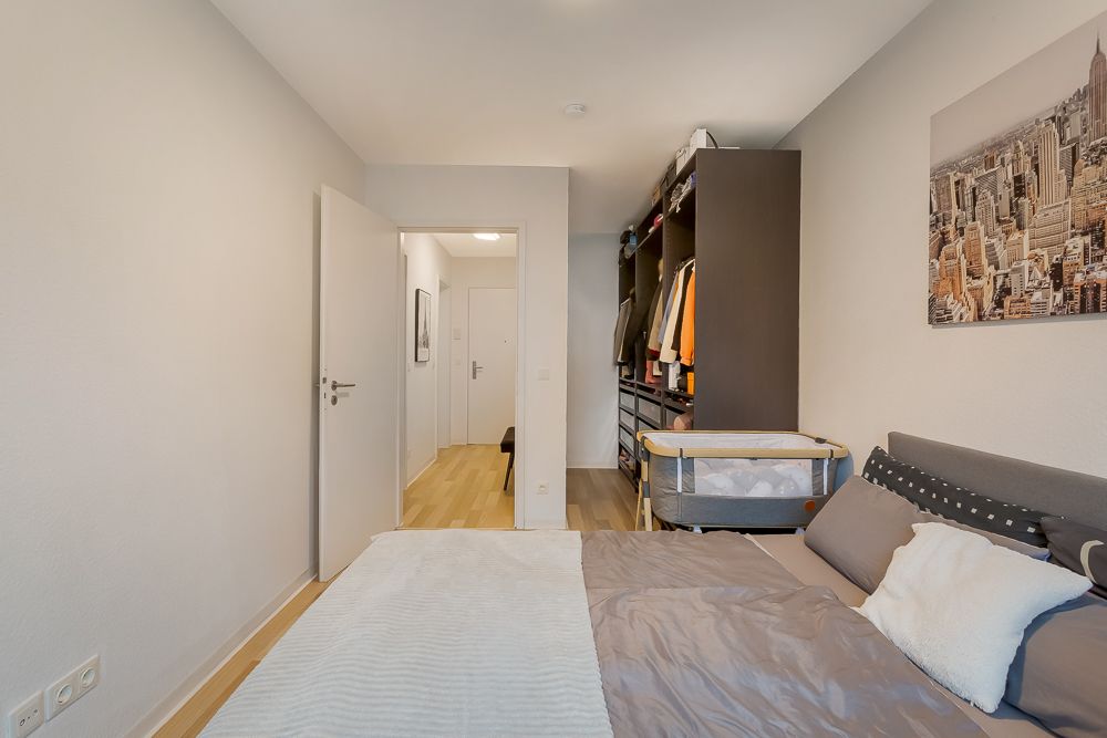 Schlafzimmer mit Bett, Babybett, offenem Kleiderschrank und Stadtbild an der Wand.