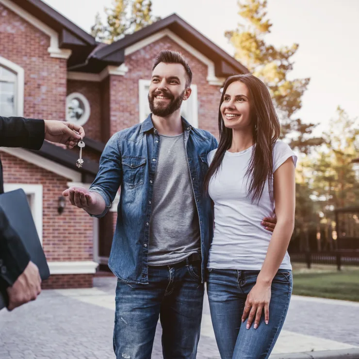Ein Mann und eine Frau erhalten vor einem Backsteinhaus einen Schlüssel von einer weiteren Person.
