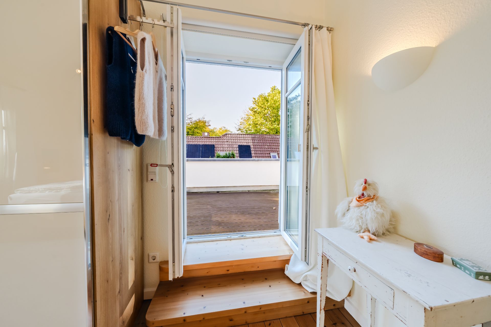 Offene Glastür mit Stufen zu einer Dachterrasse, kleiner Tisch mit Plüschgans im Raum.