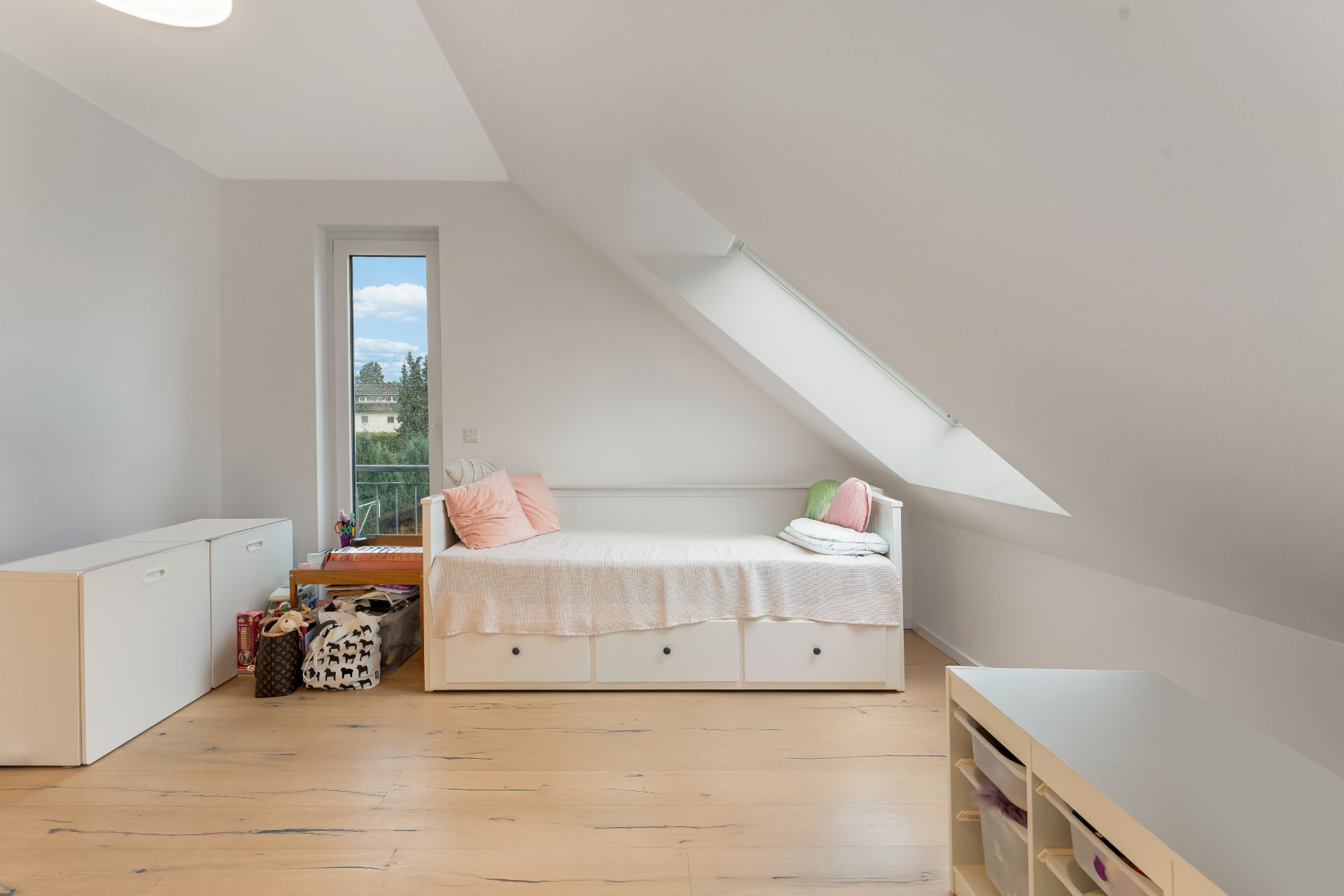 Helles Zimmer mit Einzelbett, Dachfenster, Holzfußboden und Spielzeugkisten.