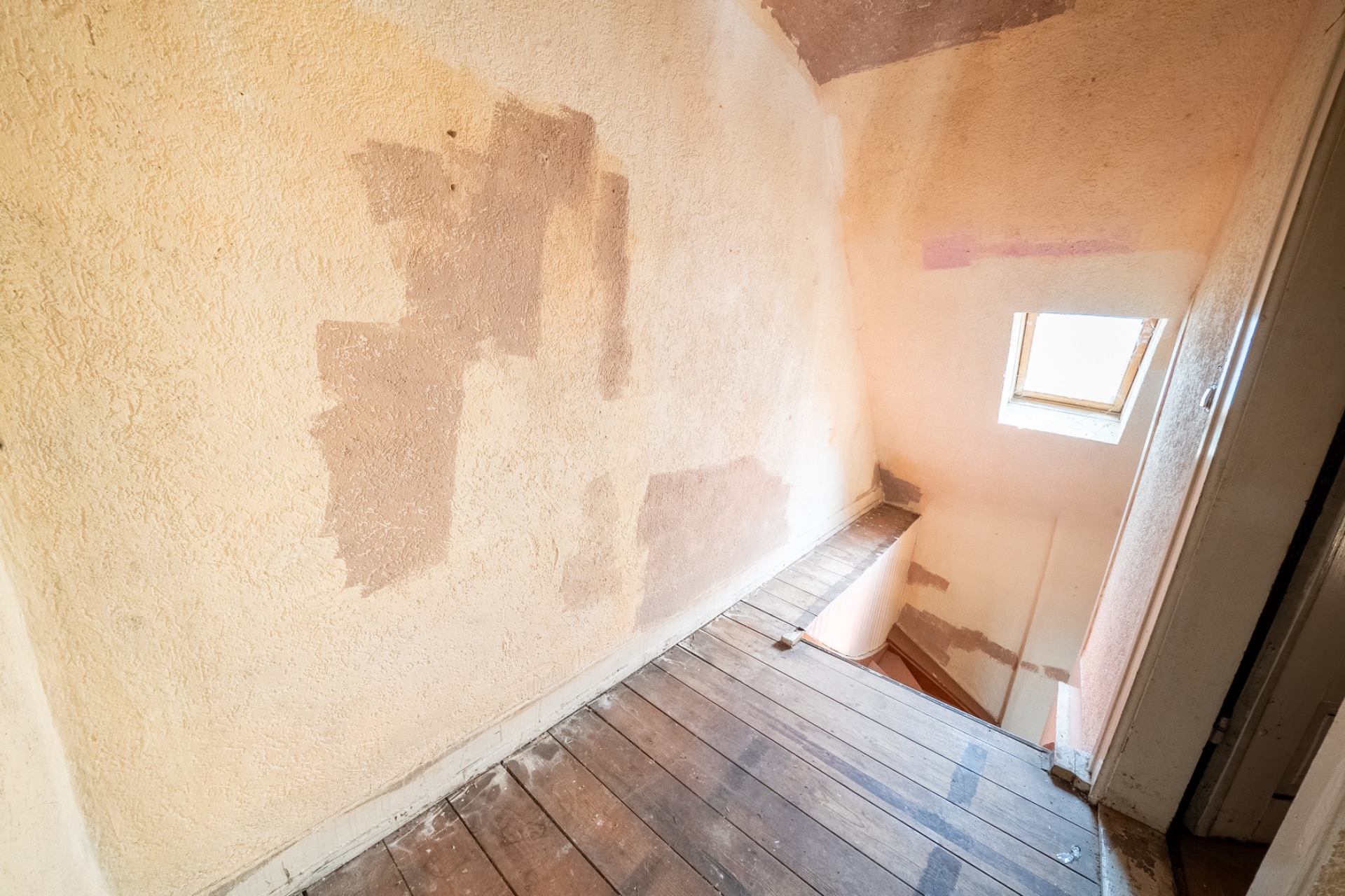 Treppe mit Holzstufen, abgenutzten Wänden und kleinem Fenster an der Wand.