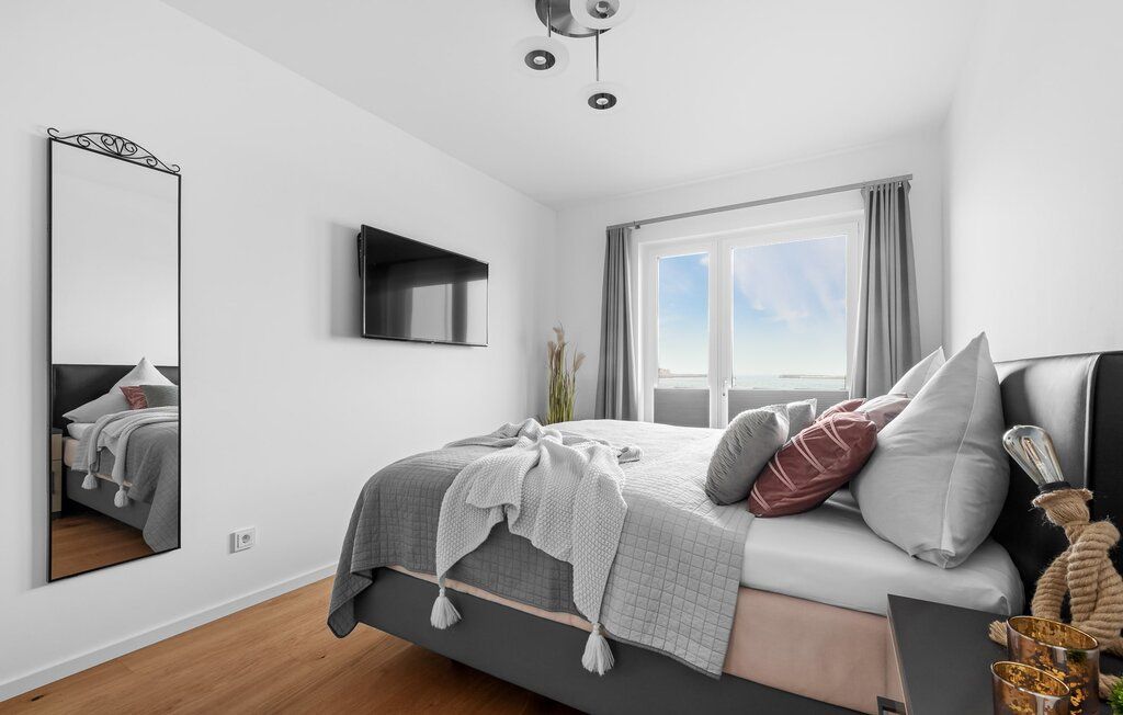 Modernes Schlafzimmer mit Doppelbett, Wandspiegel, Fernseher und Fenster mit Blick nach draußen.