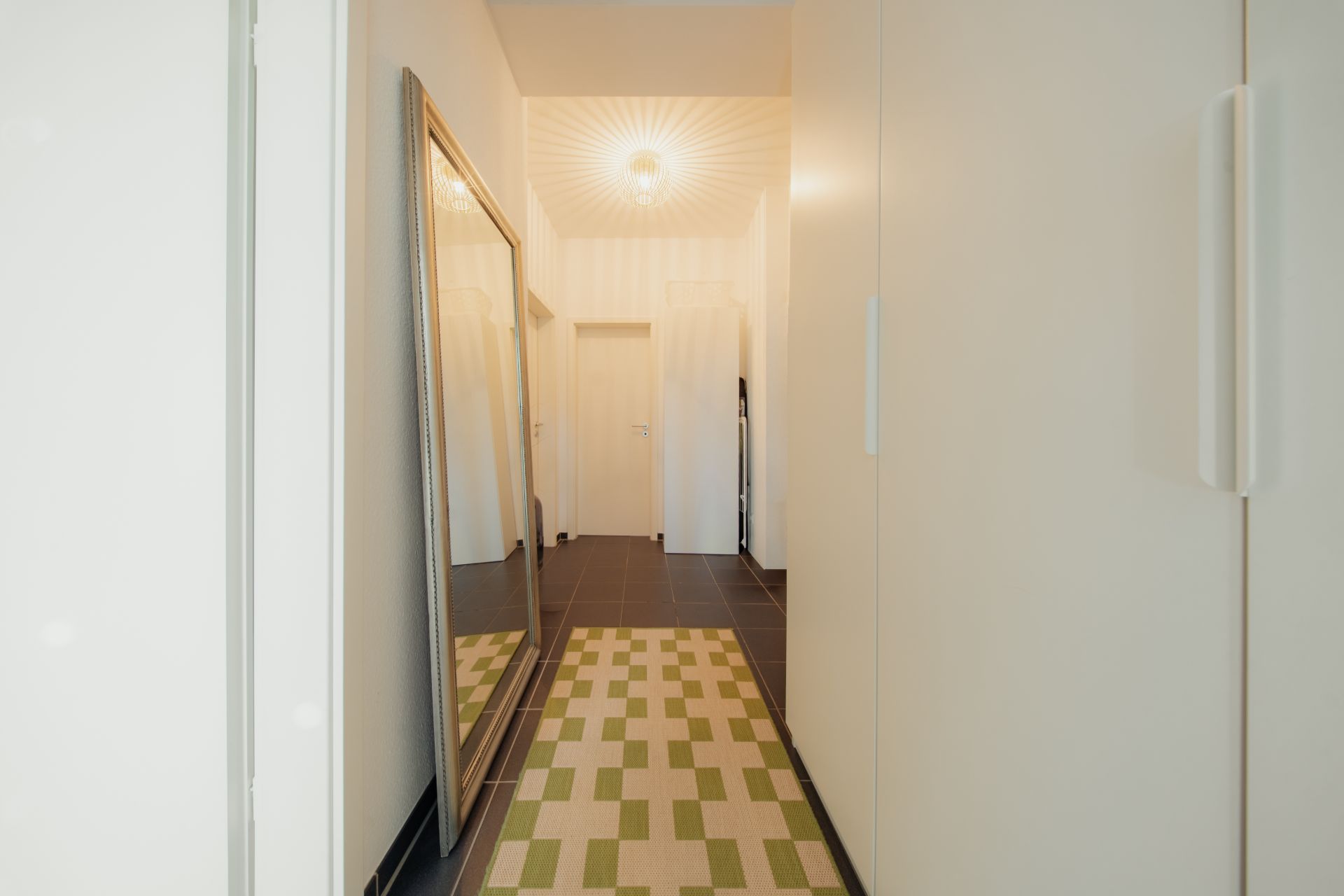 Heller Flur mit großem Spiegel, Teppich und weißen Schränken.