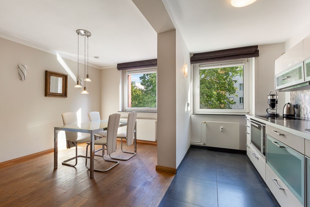 Helle Wohnküche mit Esstisch, vier Stühlen und moderner Einbauküche, große Fenster mit Blick ins Grüne.