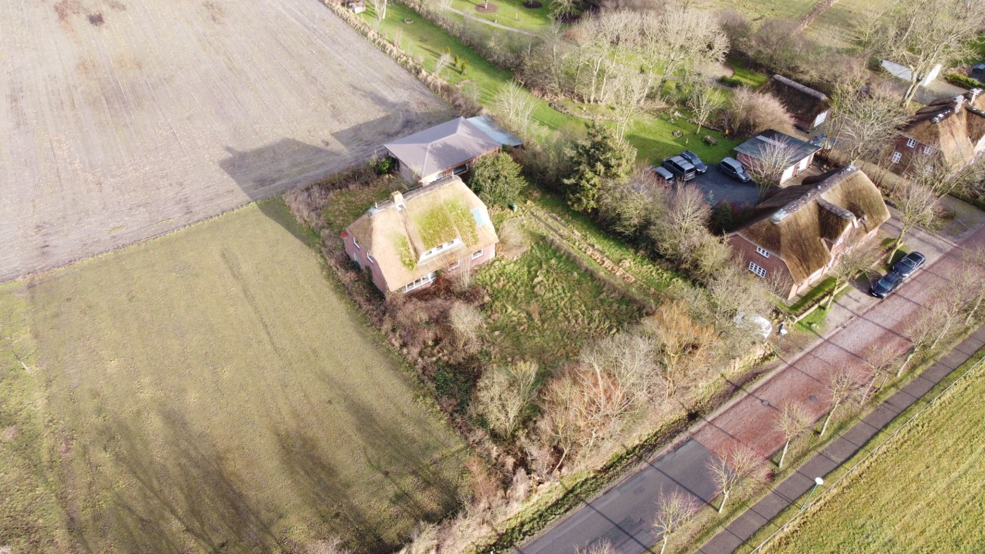 Luftaufnahme eines Hauses mit großem Garten an einer ruhigen Straße, umgeben von Feldern und weiteren Wohnhäusern.