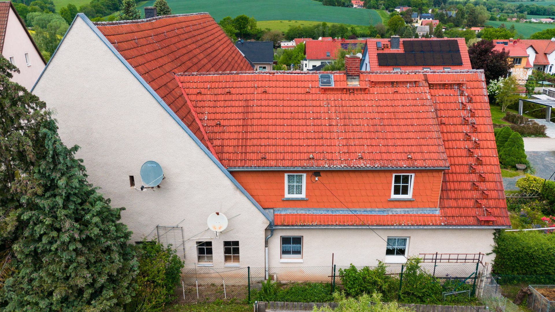 Haus mit rotem Ziegeldach, weißen Wänden und zwei Satellitenschüsseln an der Fassade.
