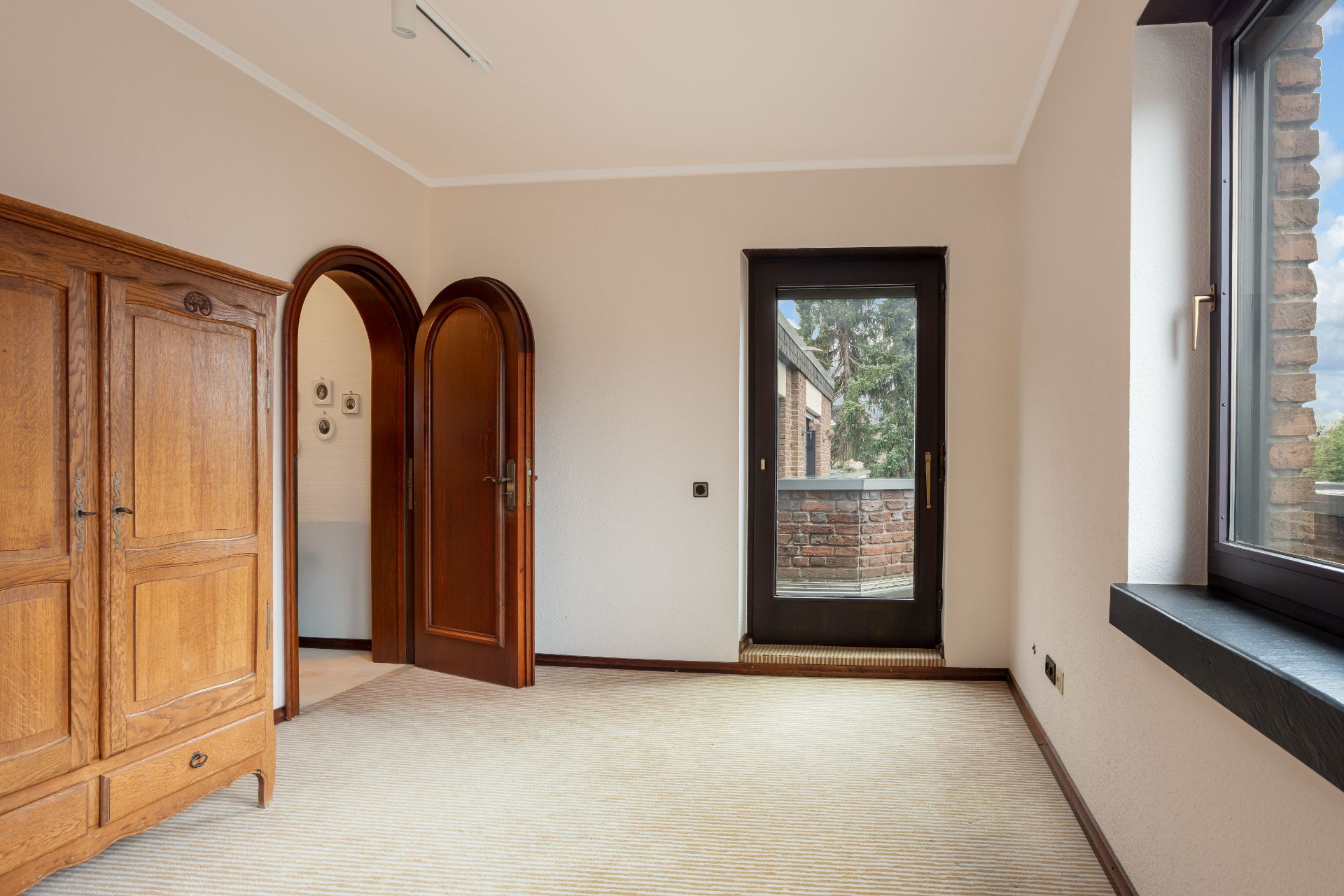 Helles Zimmer mit Holztüren, Fenster, Glastür zum Balkon und Holzschrank.