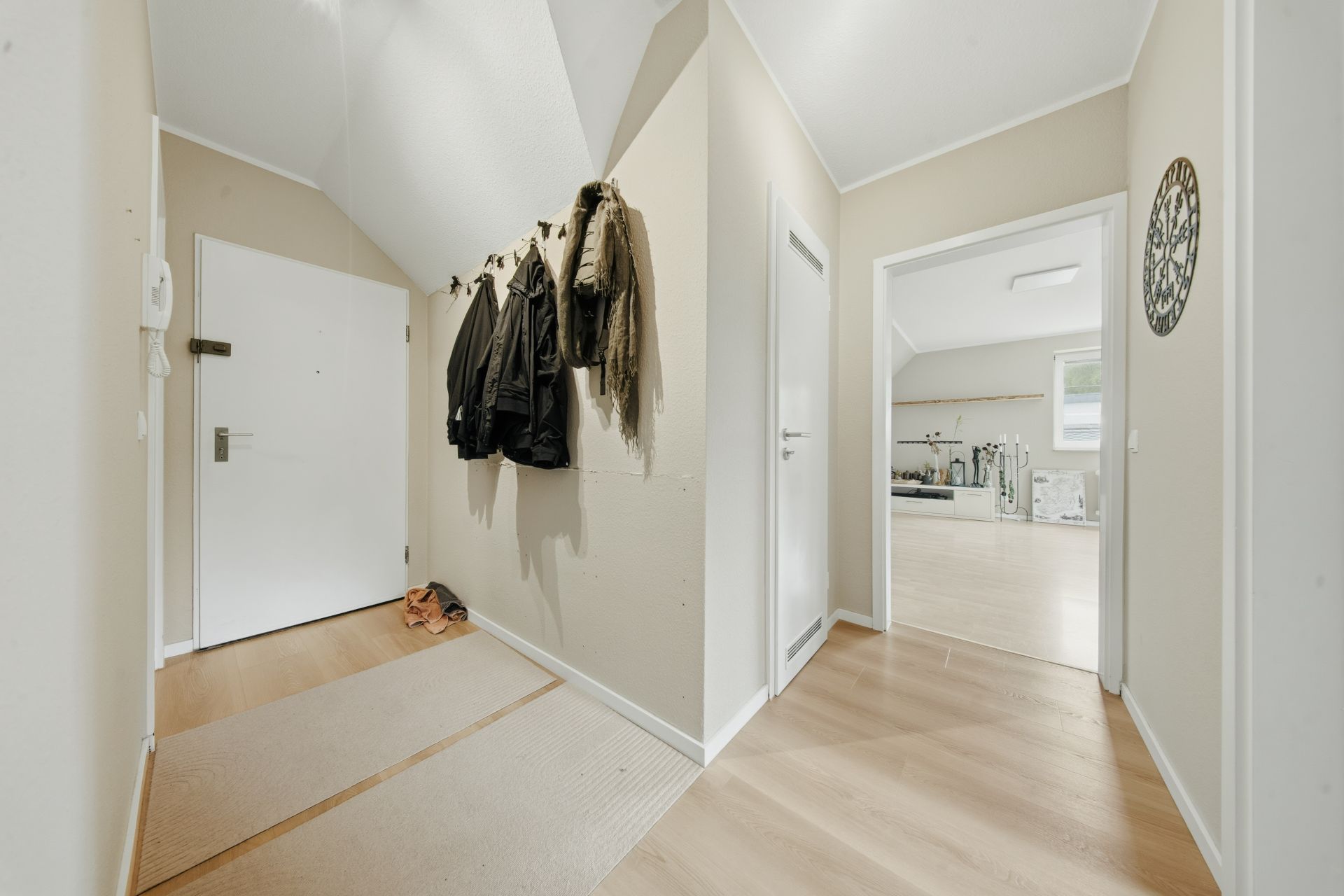 Heller Flur mit Holzboden, Garderobe mit Jacken und Zugang zu weiteren Zimmern.