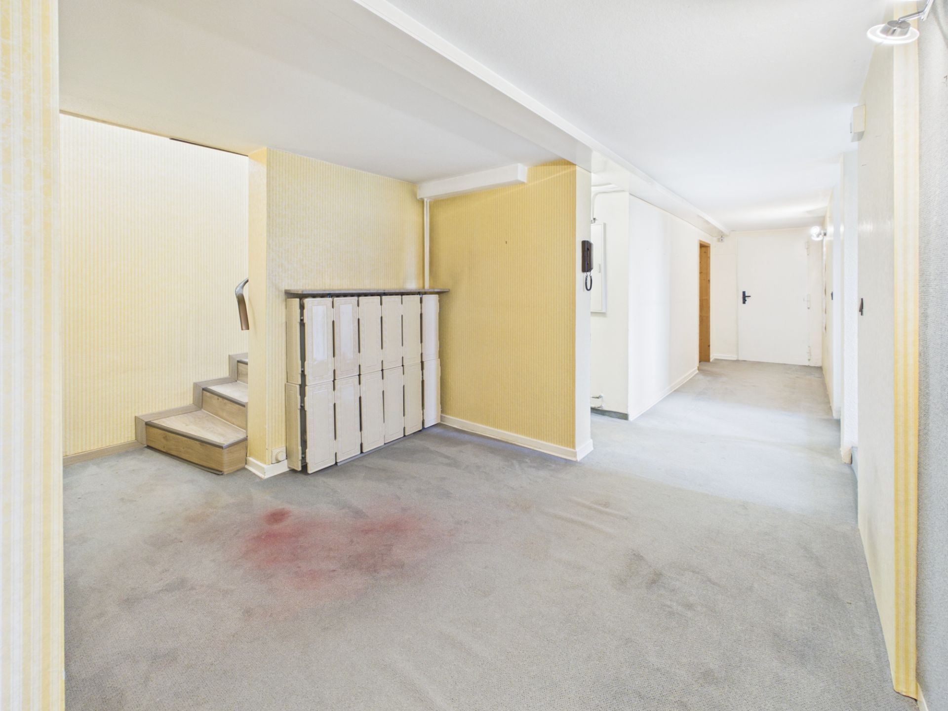 Heller Flur mit Teppichboden, gelben Wänden und einer kleinen Treppe.