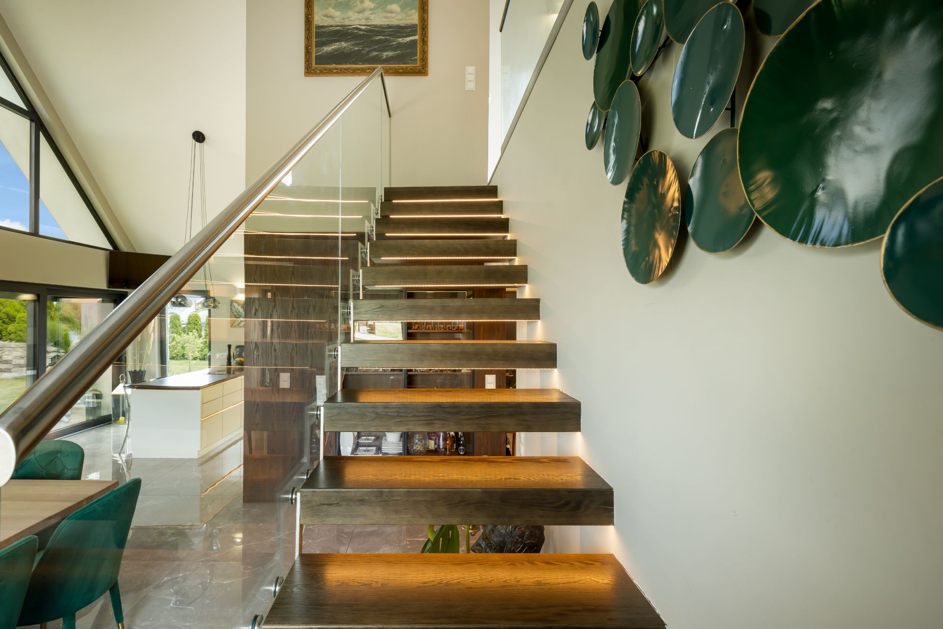 Moderne Holztreppe mit Glasgeländer und Wanddeko aus grünen Scheiben in einem hellen Wohnraum.