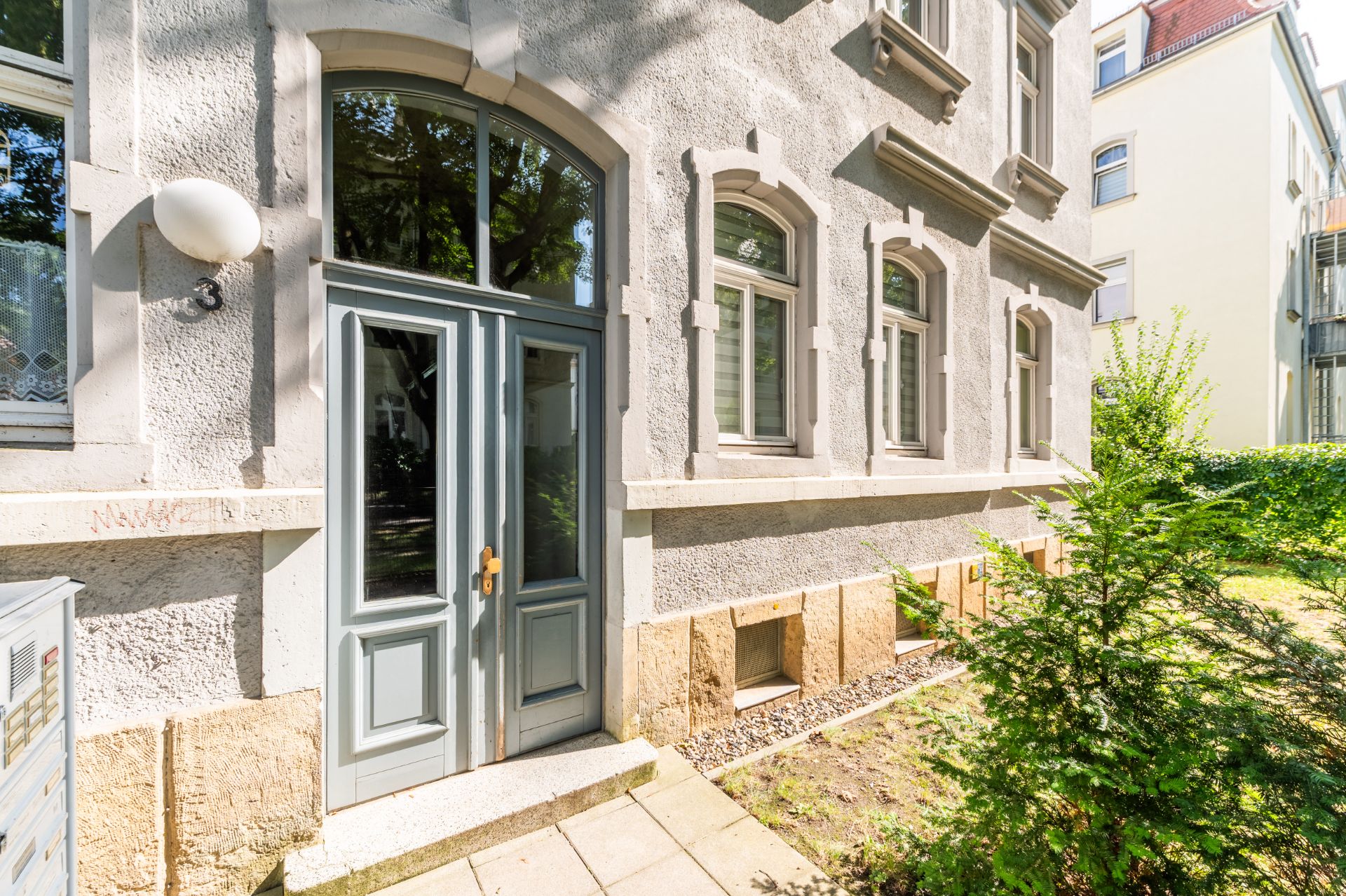 Eingangstür und Fenster eines Wohngebäudes mit Gartenbereich im Vordergrund.