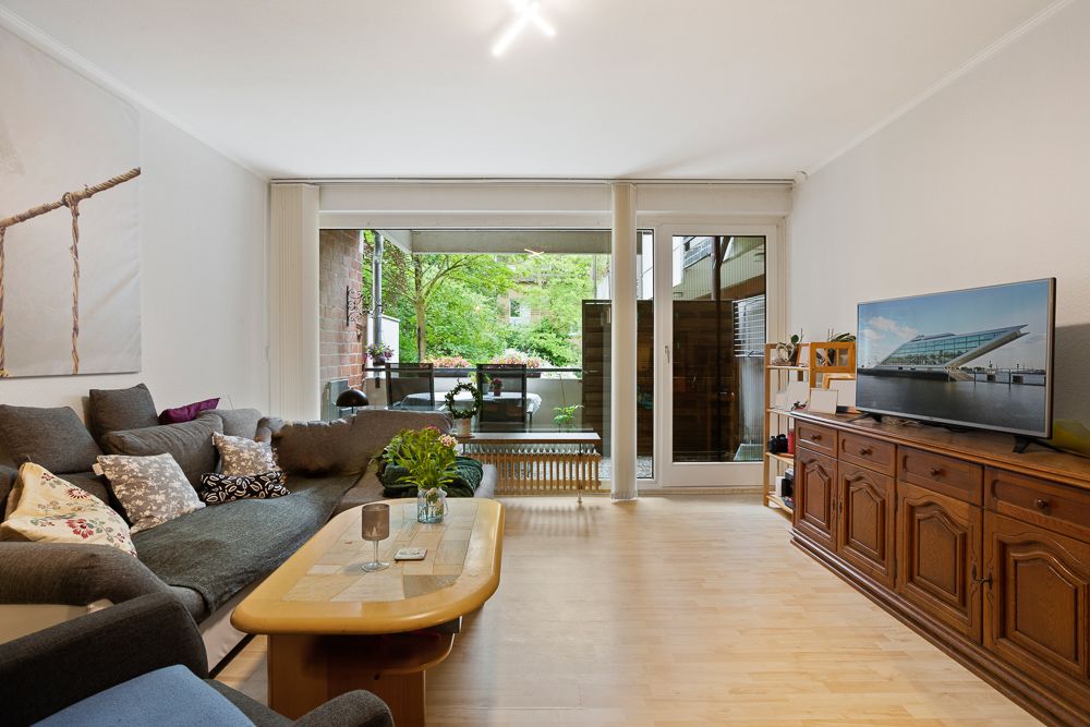 Helles Wohnzimmer mit Sofa, Couchtisch, Fernseher und Zugang zu einem Balkon mit Blick ins Grüne.