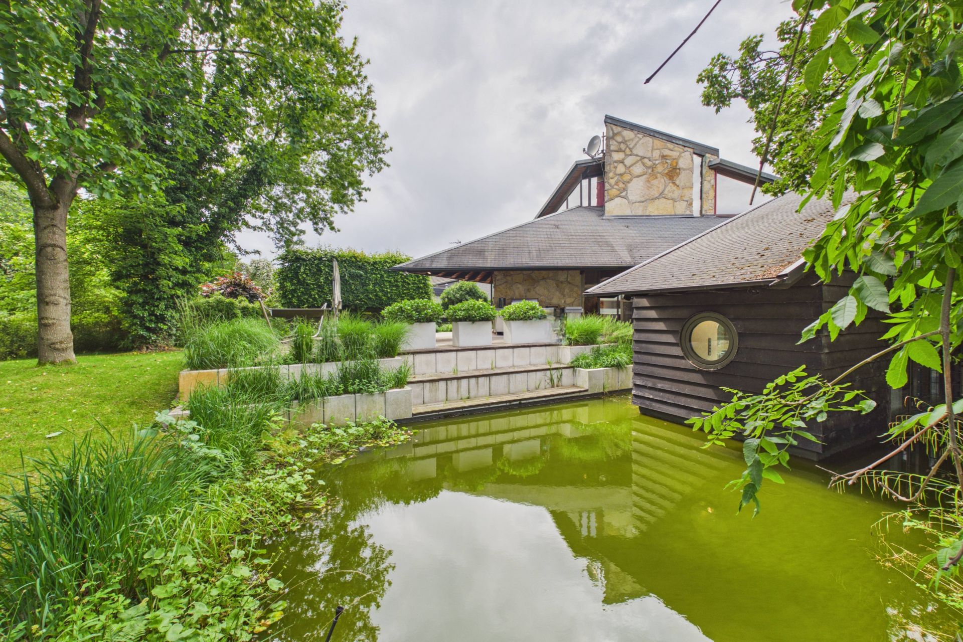 Moderner Wohnhausgarten mit Teich, Holzhaus und viel Grün.