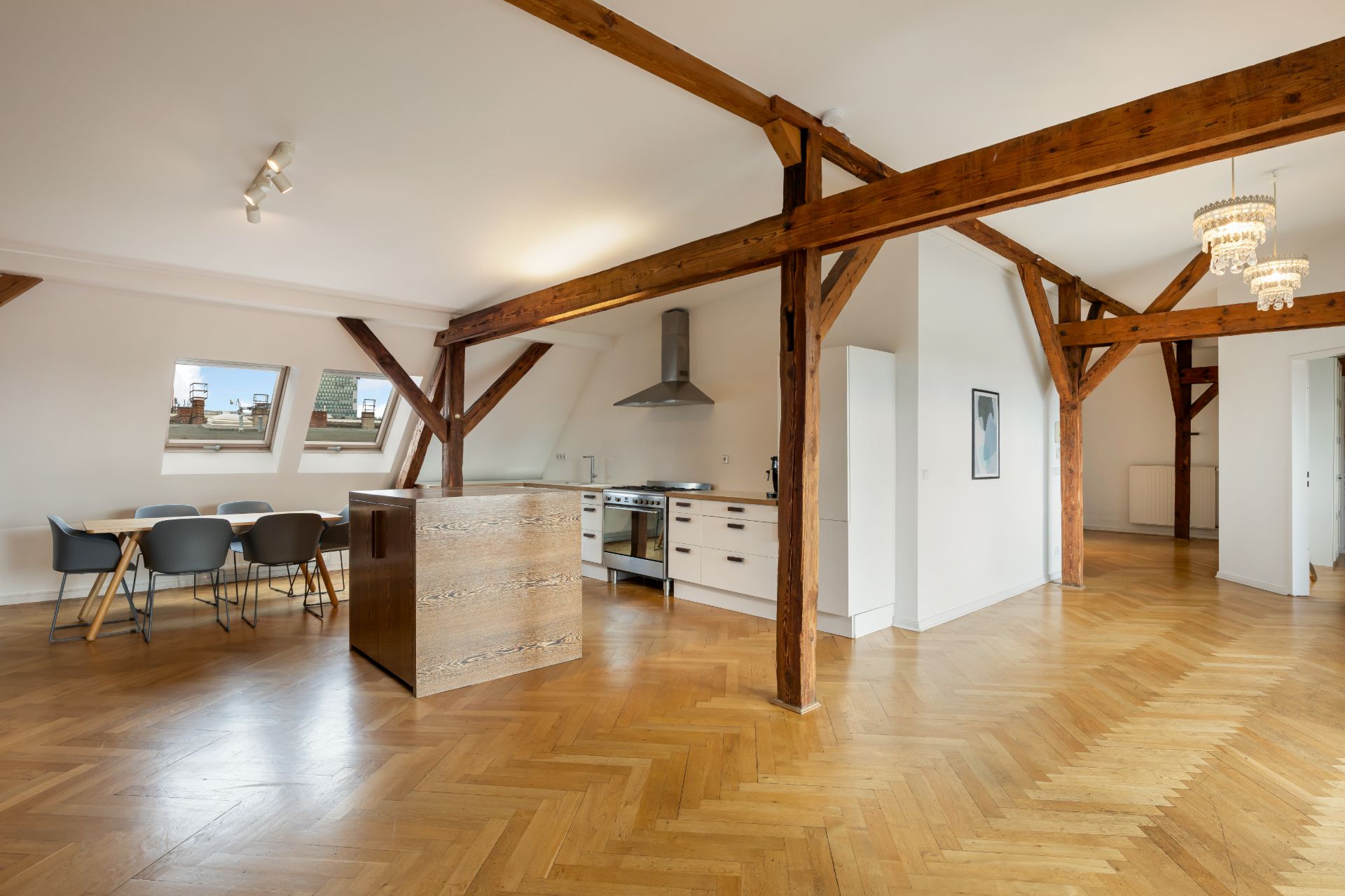 Helles Wohn- und Esszimmer mit Holzbalken, Parkettboden, Esstisch und offener Küche.