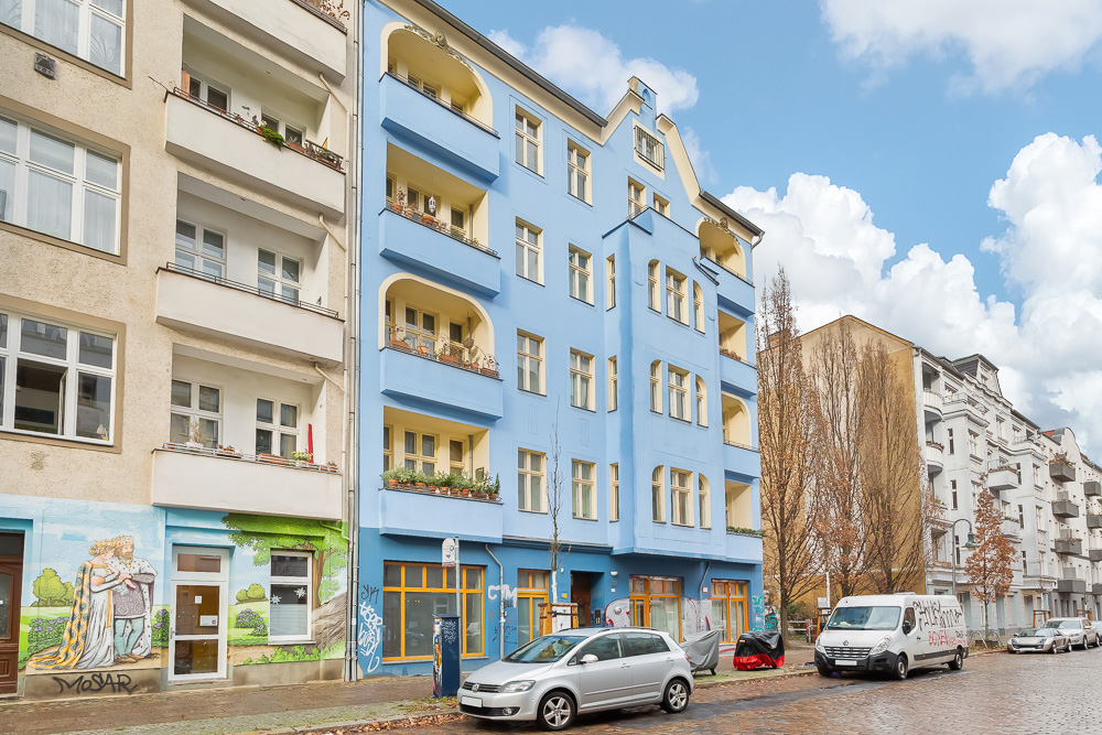 Mehrstöckiges Wohnhaus mit blauer Fassade und Balkonen an einer Straße mit geparkten Autos.