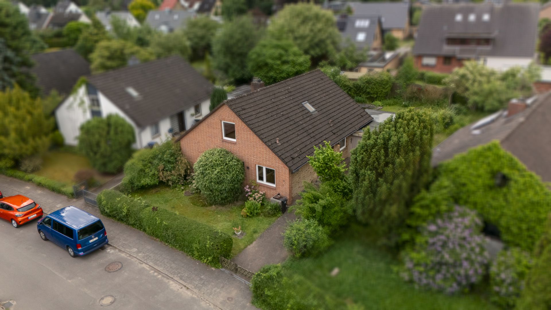 Luftaufnahme eines Einfamilienhauses mit Garten und zwei geparkten Autos an der Straße.