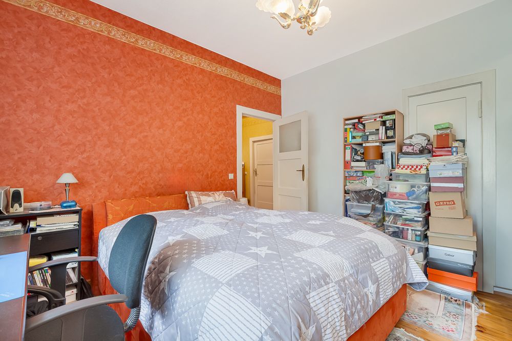 Schlafzimmer mit roter Wand, Doppelbett, Regal voller Kisten und Schreibtisch mit Stuhl.