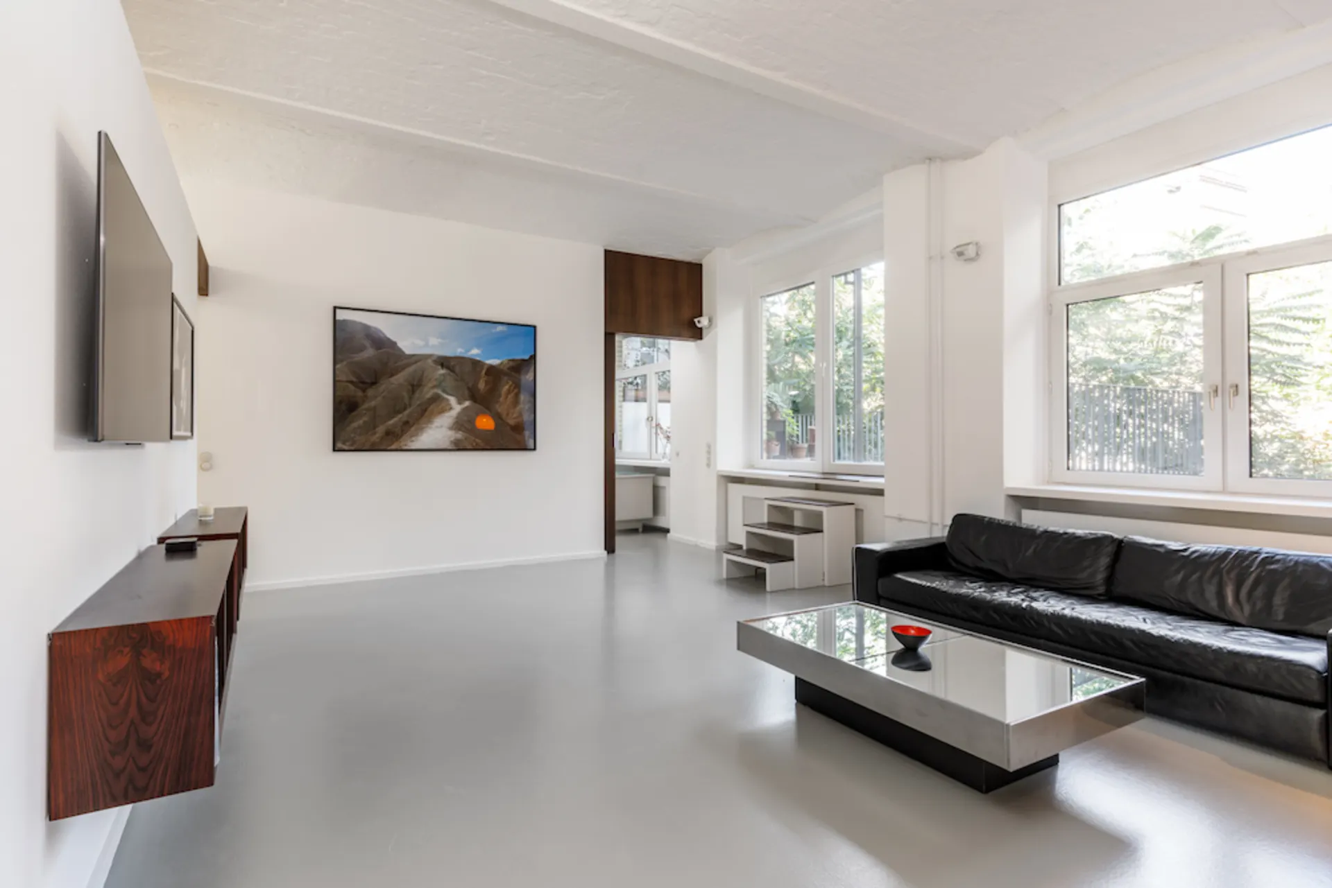 Helles Wohnzimmer mit schwarzem Sofa, Couchtisch, großem Fenster und Wandbild.