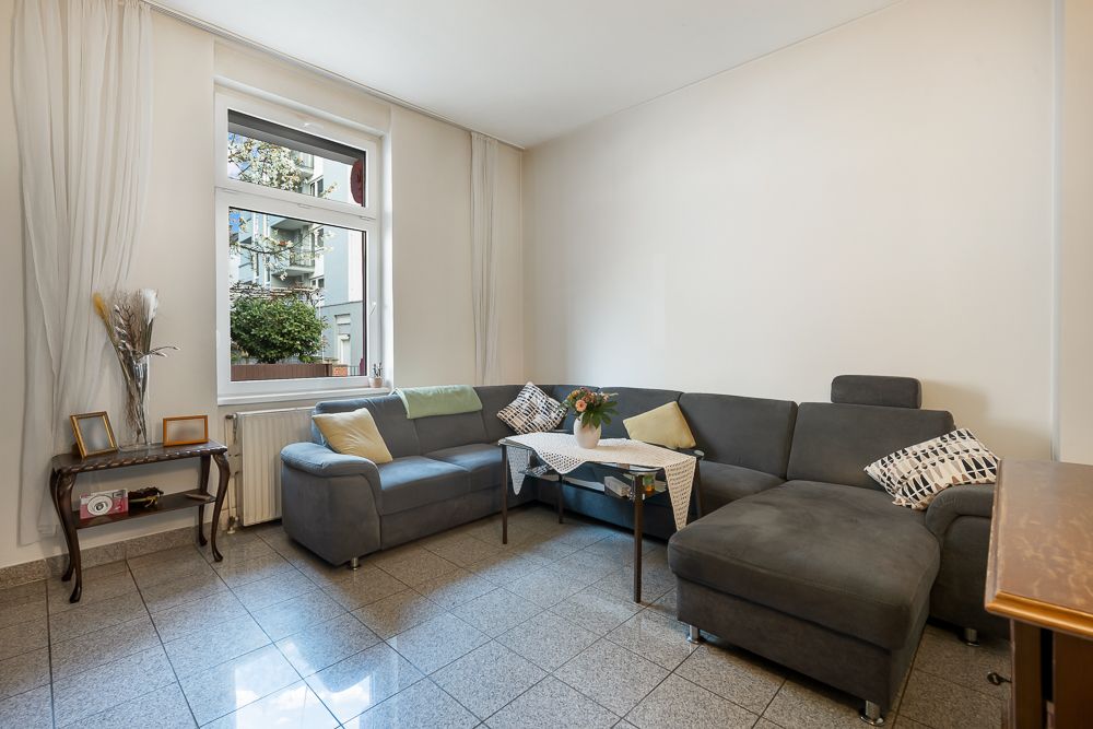 Wohnzimmer mit grauem Ecksofa, Couchtisch, Fenster und Fliesenboden.