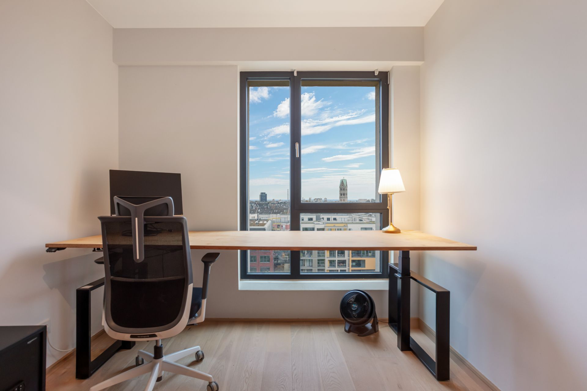 Helles Arbeitszimmer mit Schreibtisch, Bürostuhl, Monitor und Fenster mit Stadtblick.