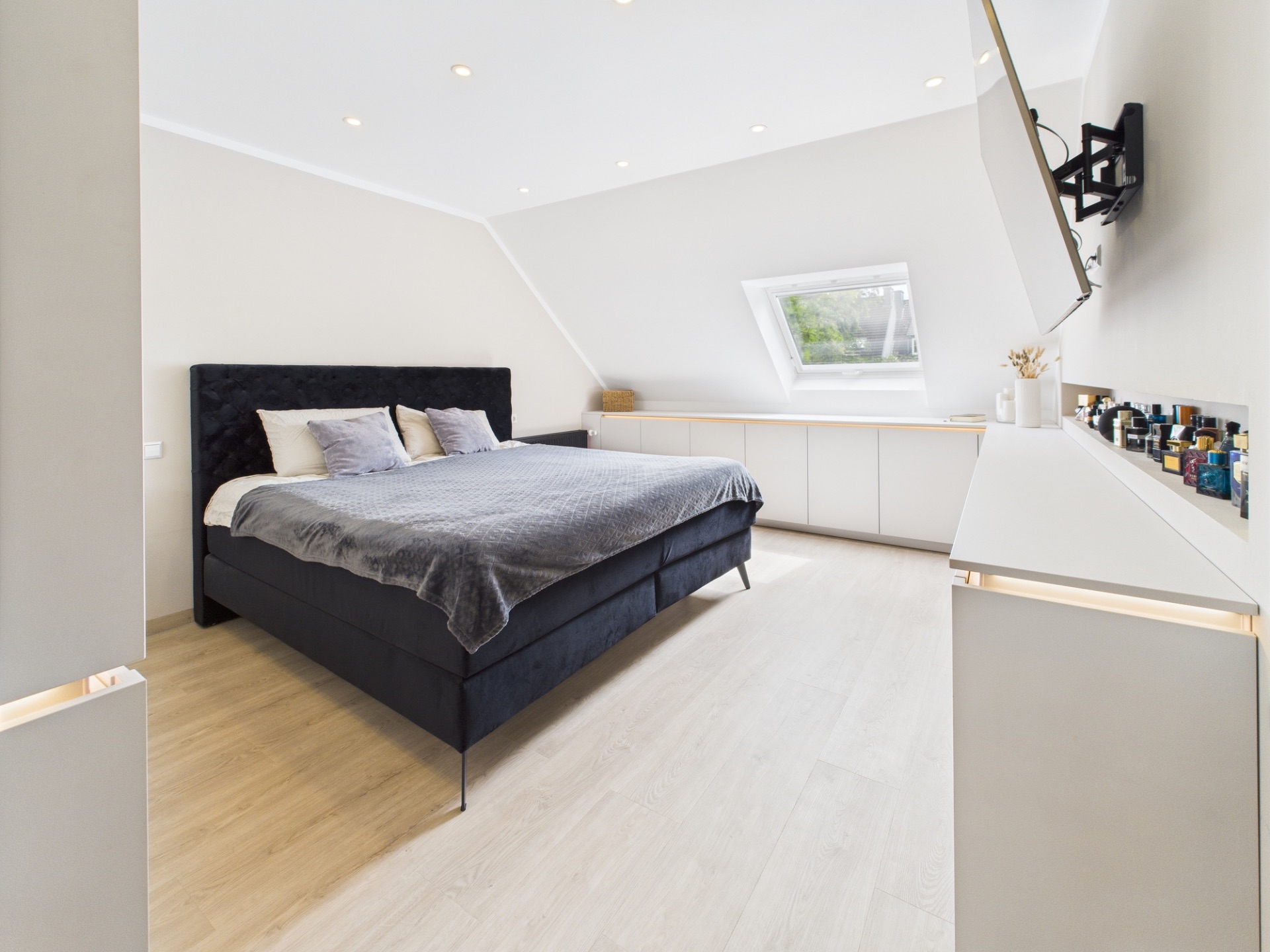Modernes Schlafzimmer mit Doppelbett, Fernseher an der Wand und Fenster in der Schräge.