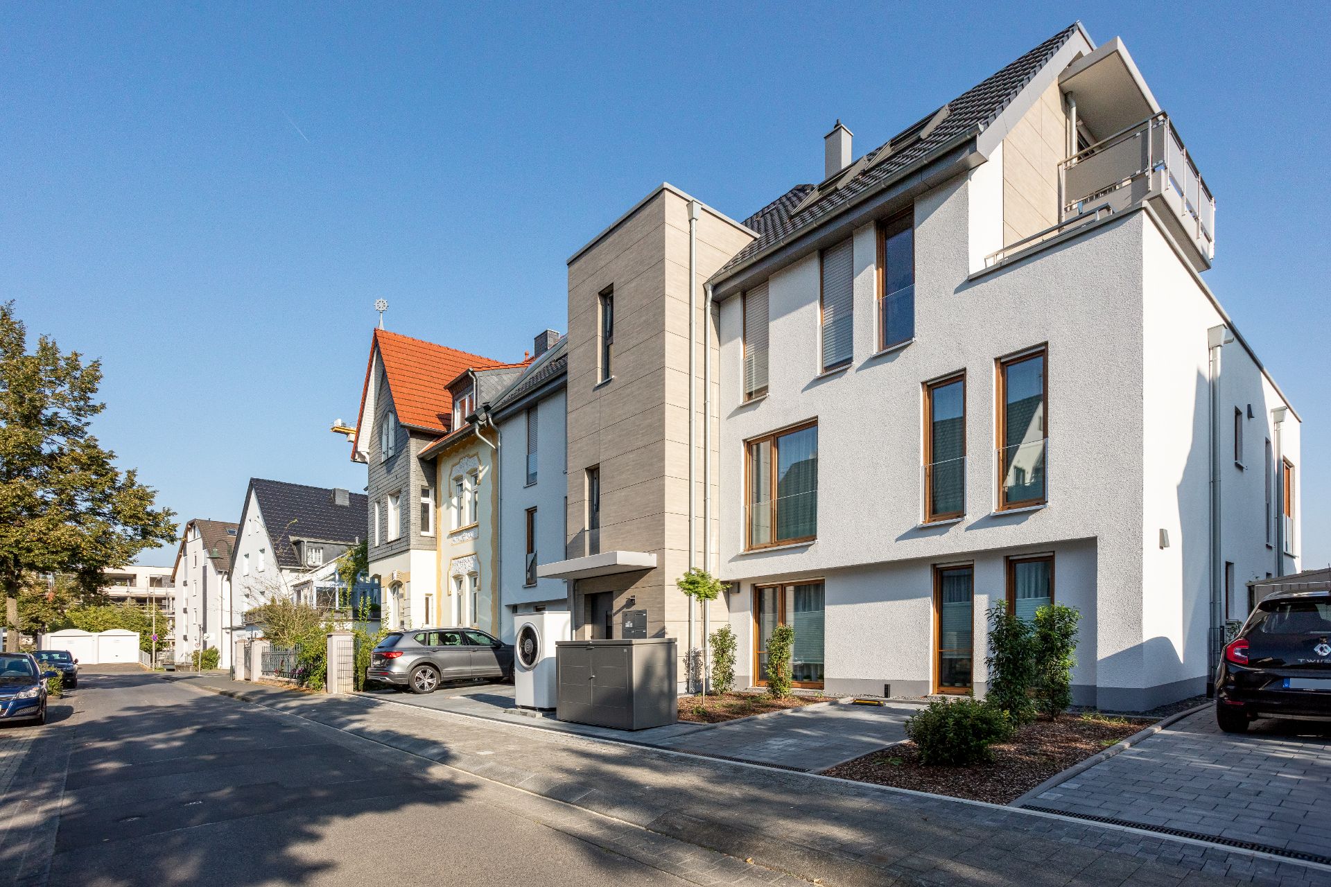 Modernes Wohnhaus mit mehreren Stockwerken und großen Fenstern an einer ruhigen Straße.