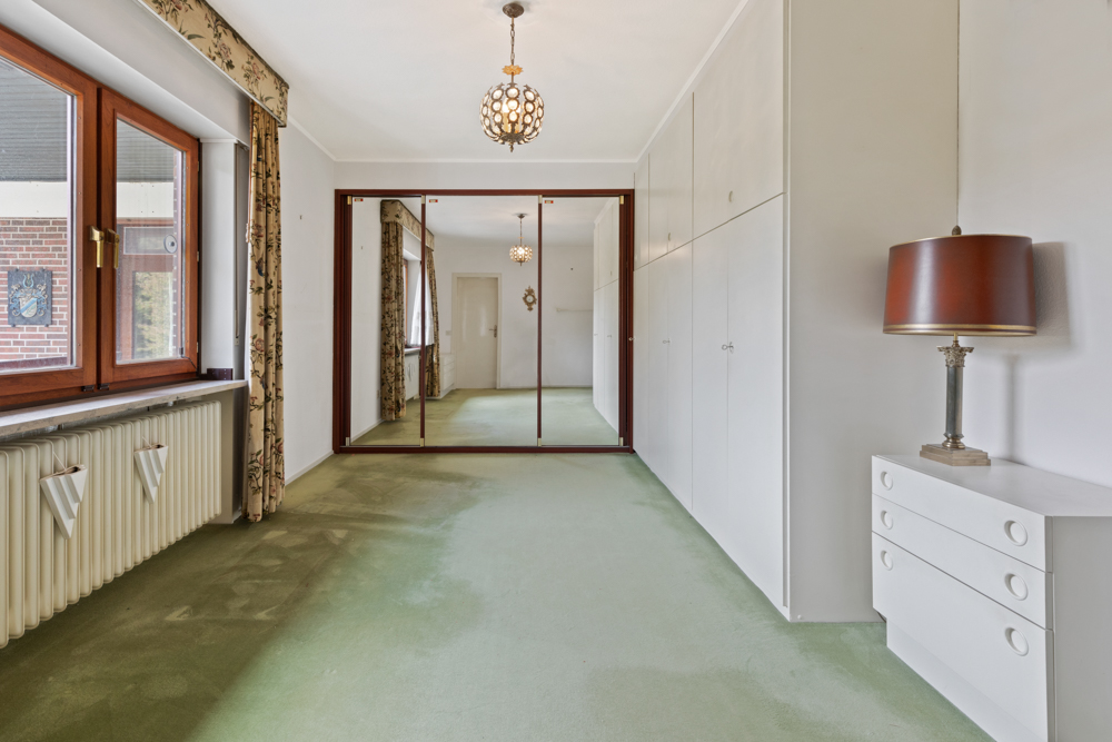 Schlafzimmer mit grünem Teppich, großen Spiegeln, weißen Einbauschränken und einer Kommode mit Lampe.