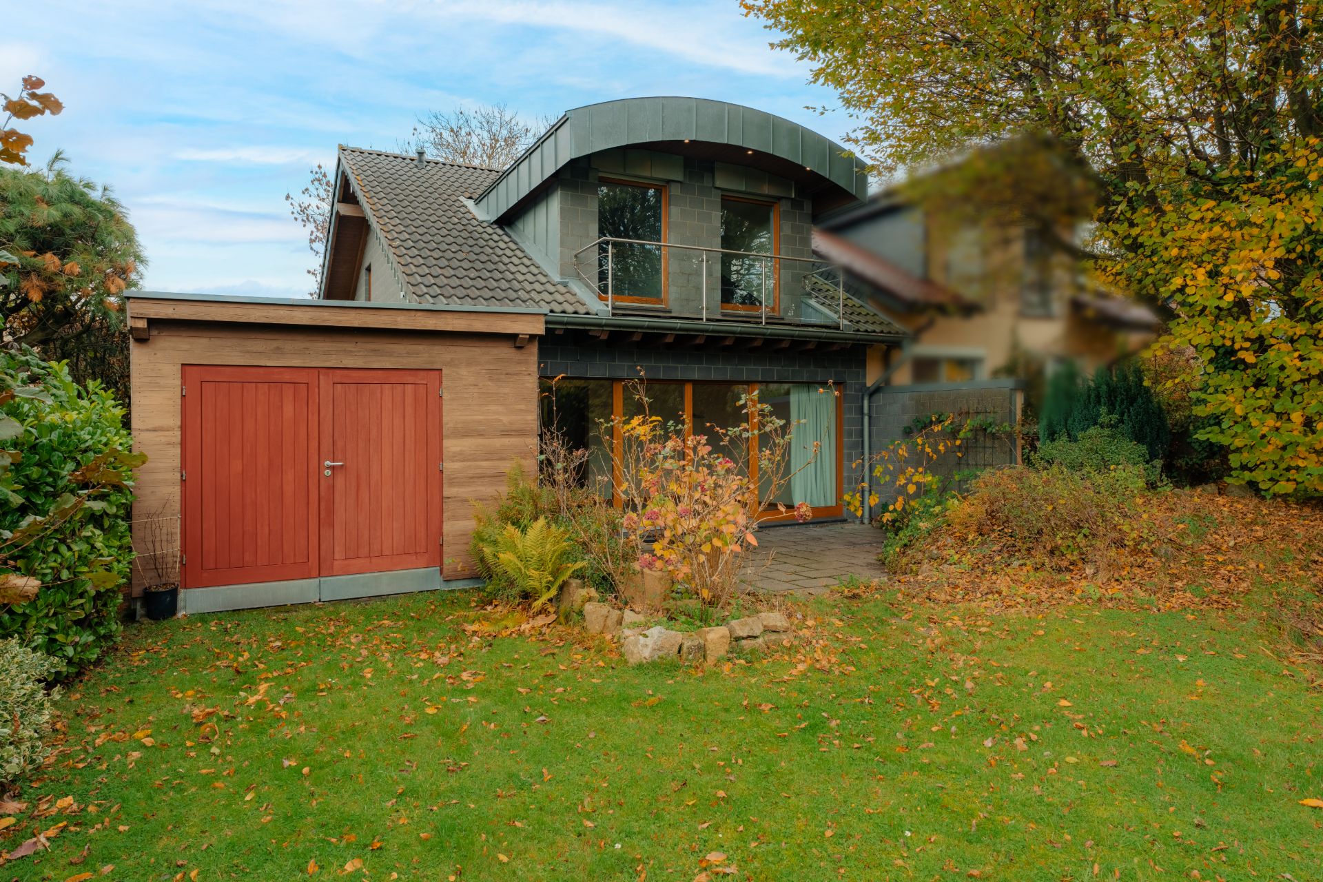 Zweistöckiges Haus mit Balkon, Garage und Garten, umgeben von Bäumen und Herbstlaub.