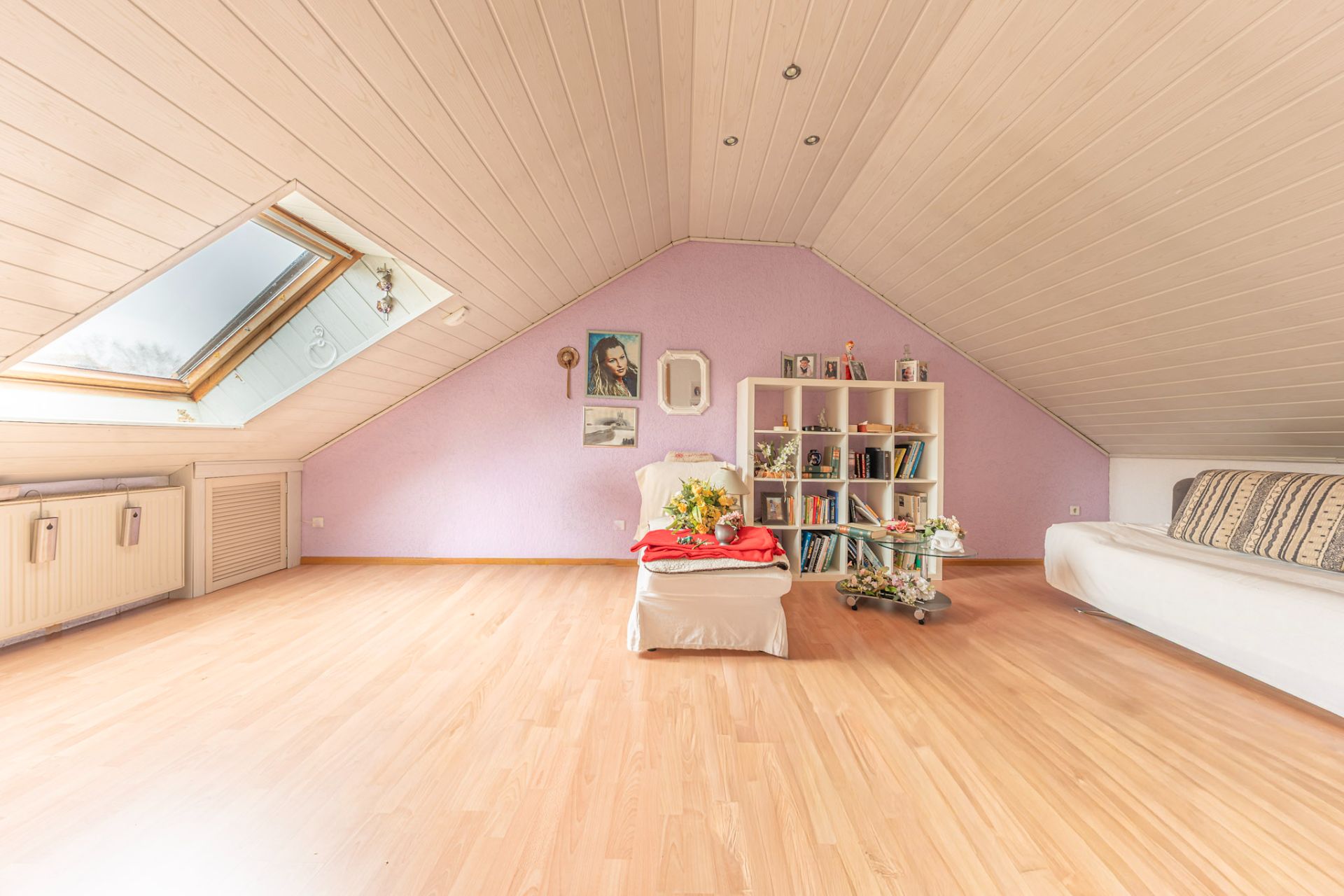 Heller Dachbodenraum mit Holzdecke, Sessel, Regal, Sofa und Dachfenster.