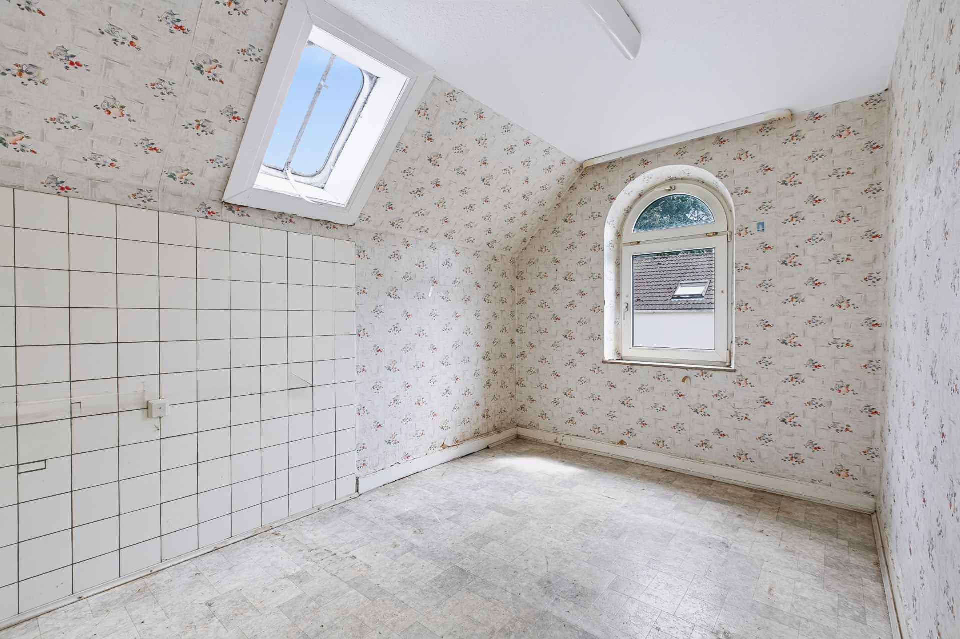 Leerer Raum mit Dachfenster, Fliesenwand und gebogenem Fenster, geblümte Tapete.