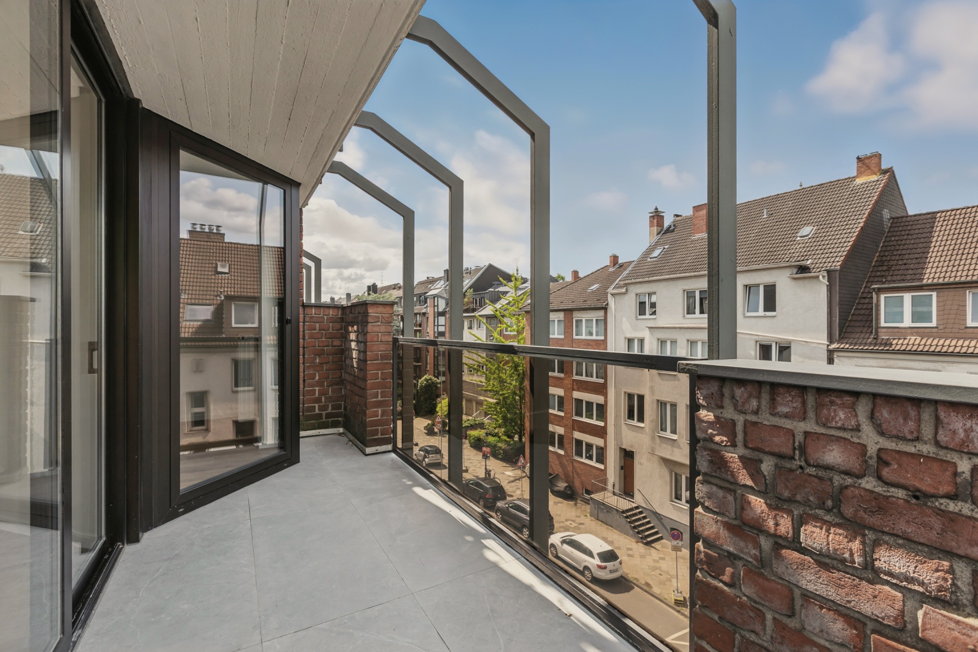 Balkon mit Glasgeländer und Blick auf eine ruhige Wohnstraße mit Häusern.