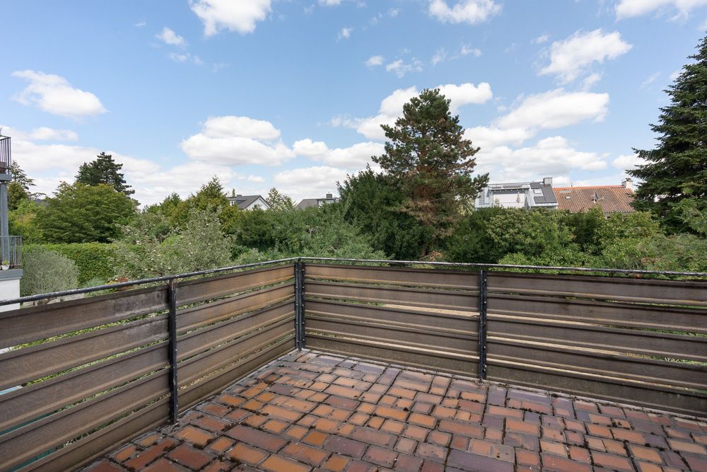 Balkon mit Holzgeländer und Blick auf Bäume und Häuser im Hintergrund.
