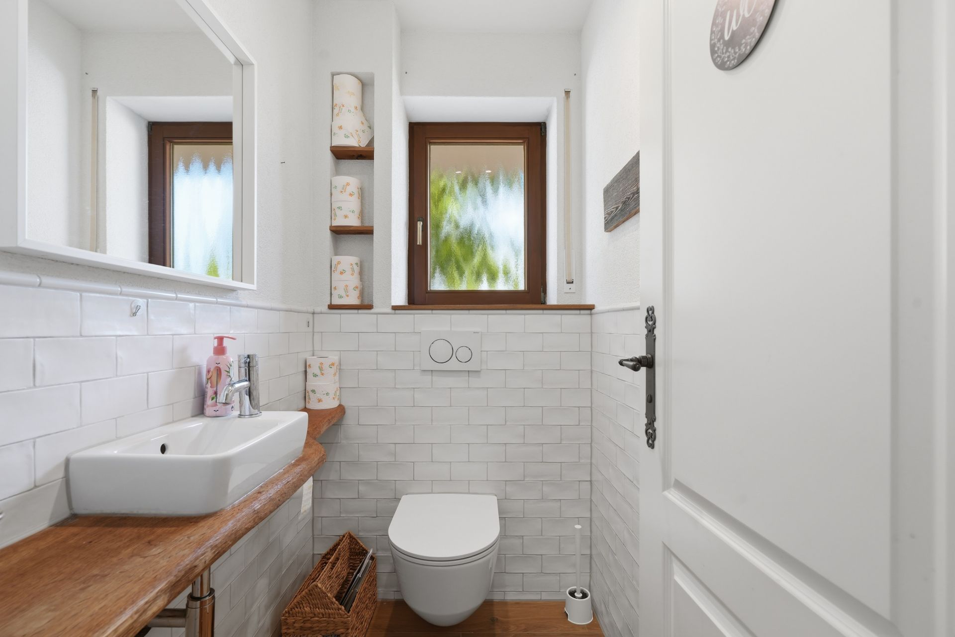 Modernes kleines Badezimmer mit Wandtoilette, Waschbecken, Fenster und Regal mit Toilettenpapier.