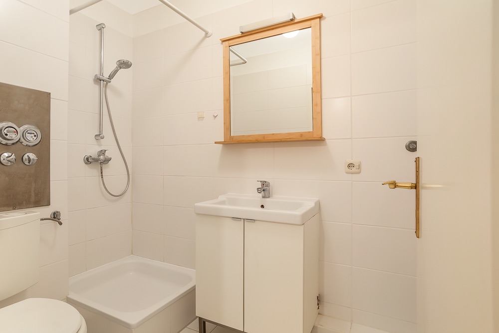 Modernes Badezimmer mit Dusche, Waschbecken, Spiegel und Toilette, alles in weiß gehalten.