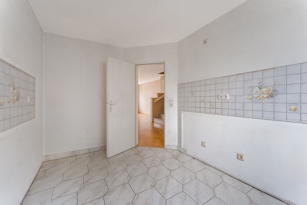 Leerer Raum mit weißen Fliesen, offenen Tür und gefliester Wand mit Blumenmotiven.