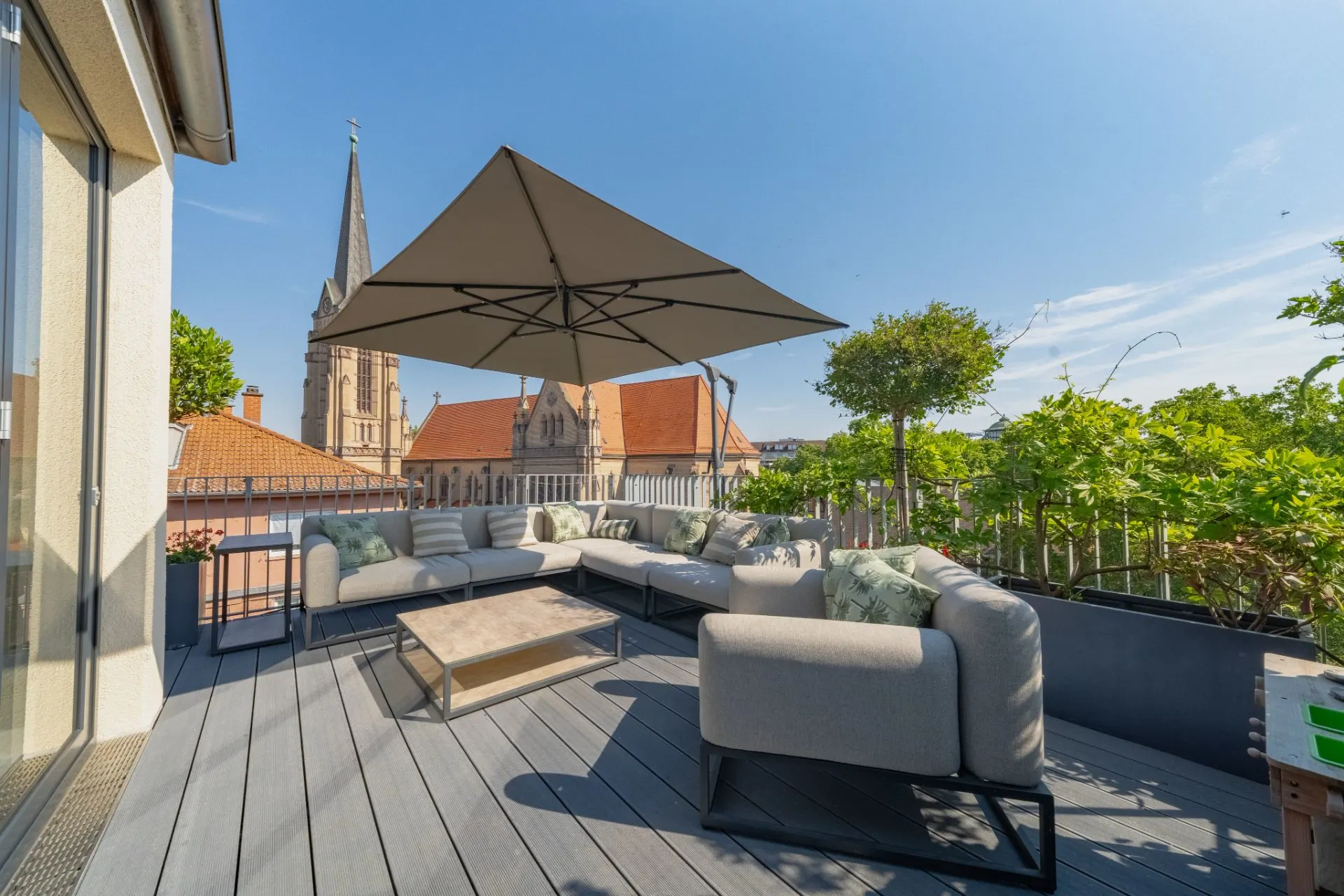 Große Dachterrasse mit Sitzgruppe, Tisch und Sonnenschirm, im Hintergrund Kirche.