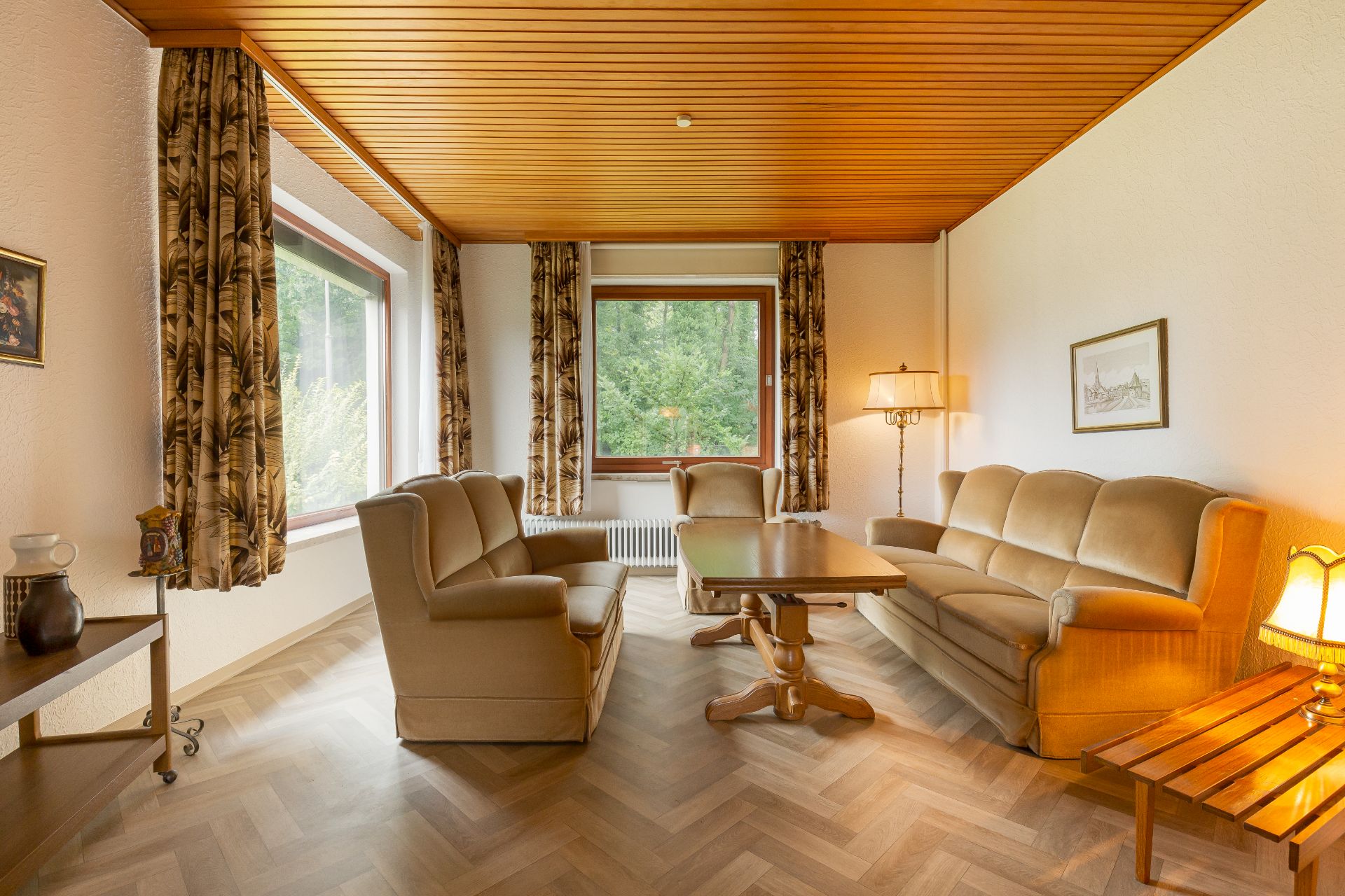 Wohnzimmer mit beigen Sofas, Holzdecke, großem Fenster und Stehlampe.
