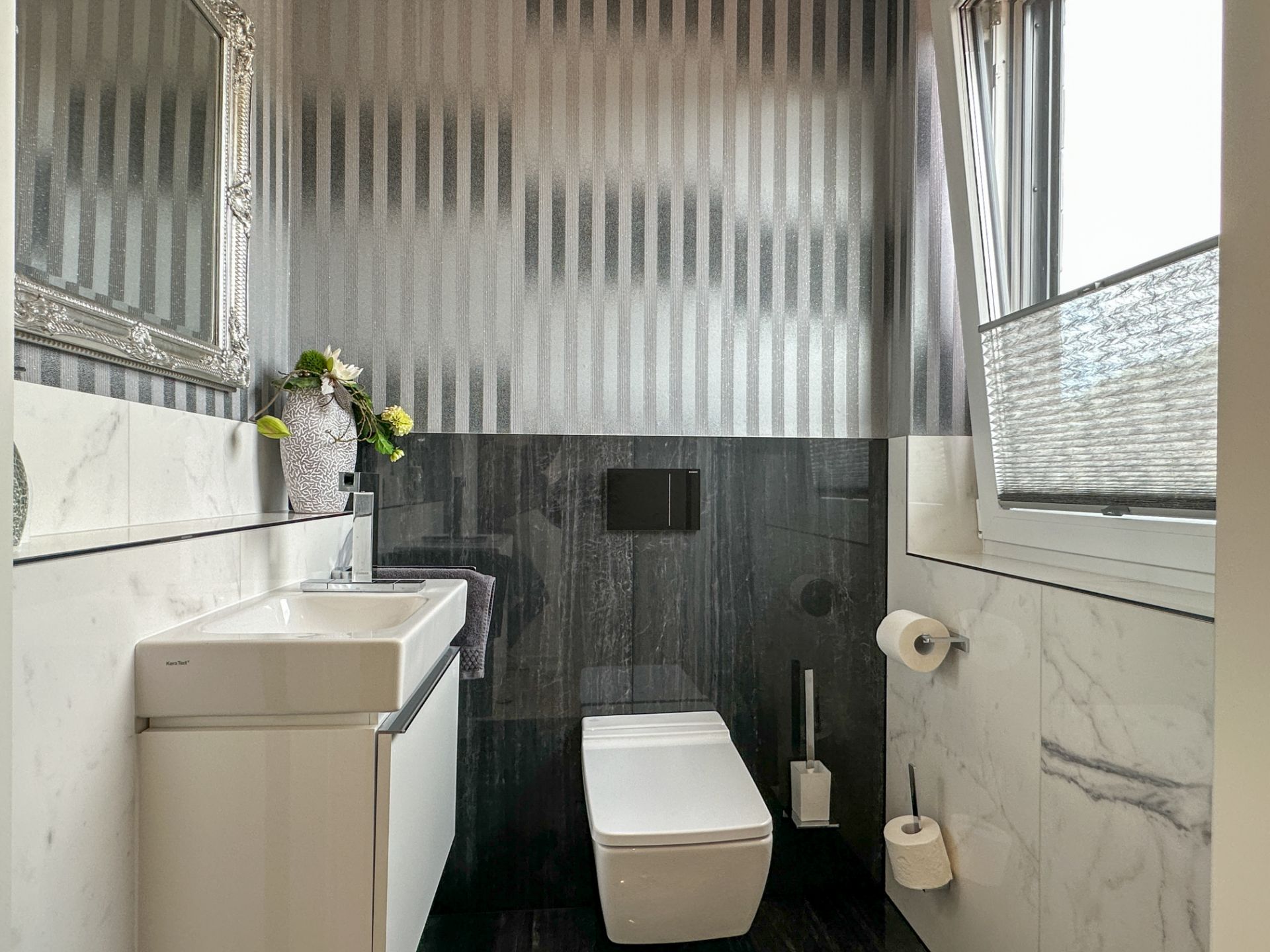 Modernes Badezimmer mit Wandtoilette, Waschbecken, Spiegel und geöffnetem Fenster.