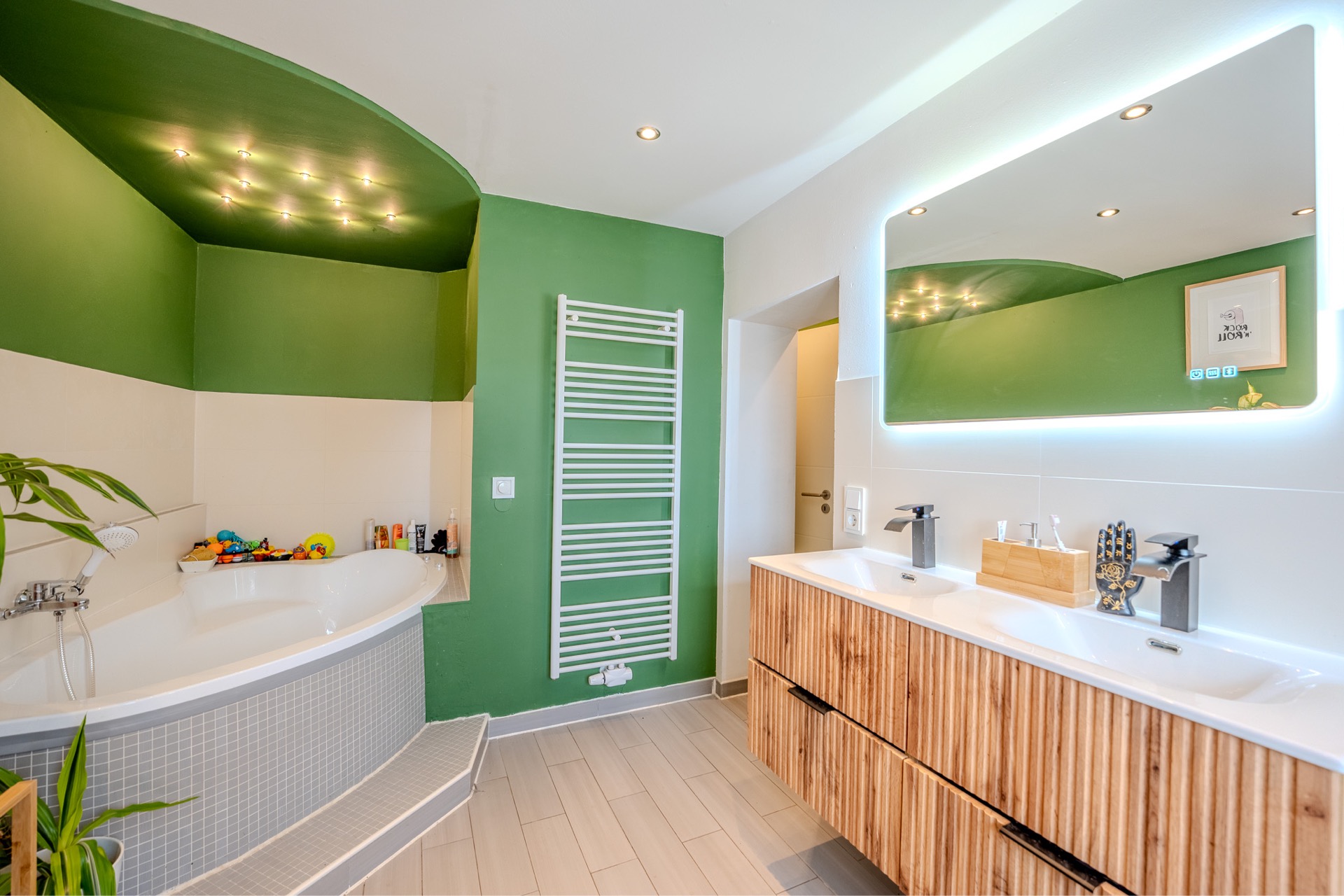 Modernes Badezimmer mit Eckbadewanne, Doppelwaschbecken und grün gestrichenen Wänden.