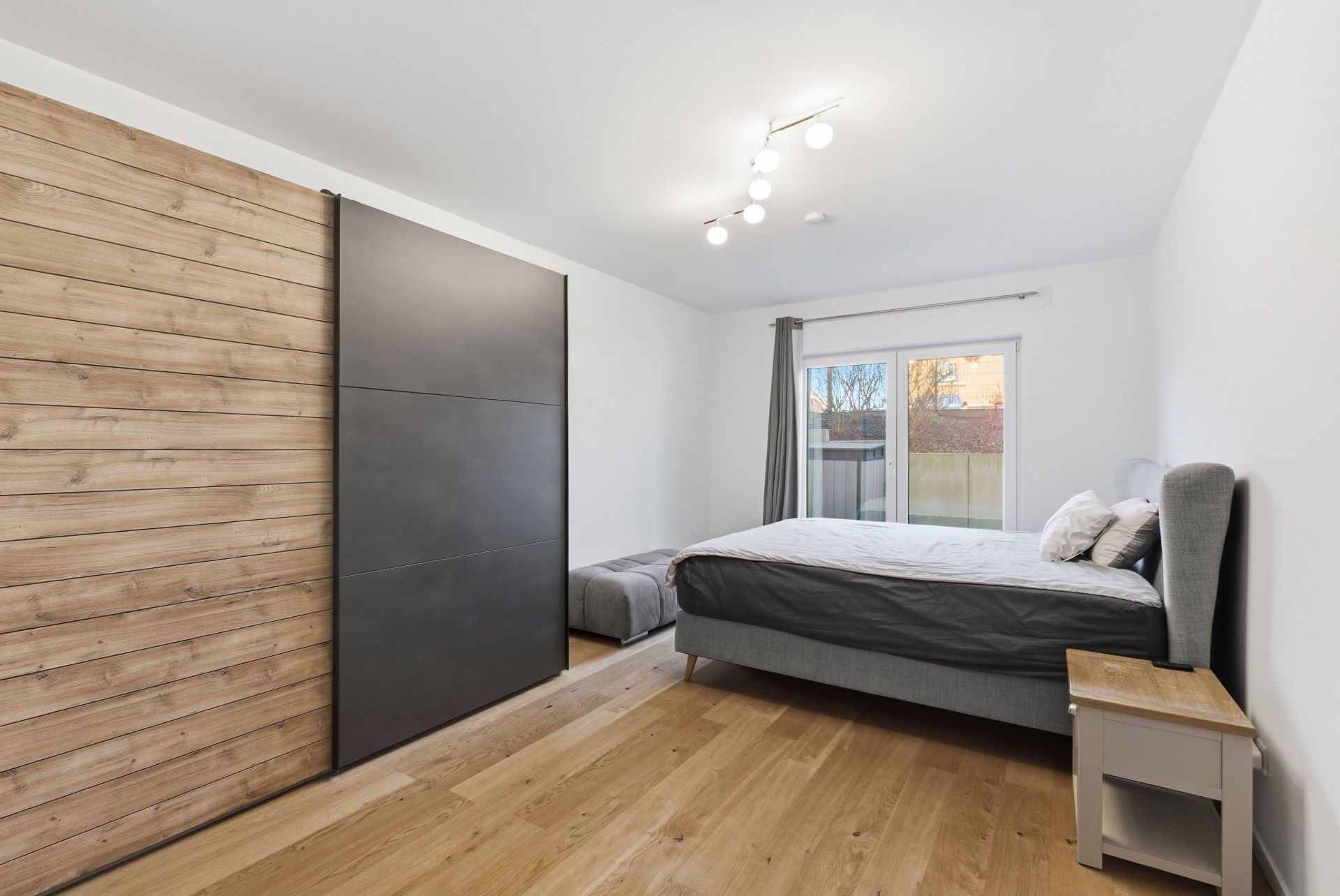Modernes Schlafzimmer mit Bett, Nachttisch, großem Schrank und Fenster mit Vorhängen.