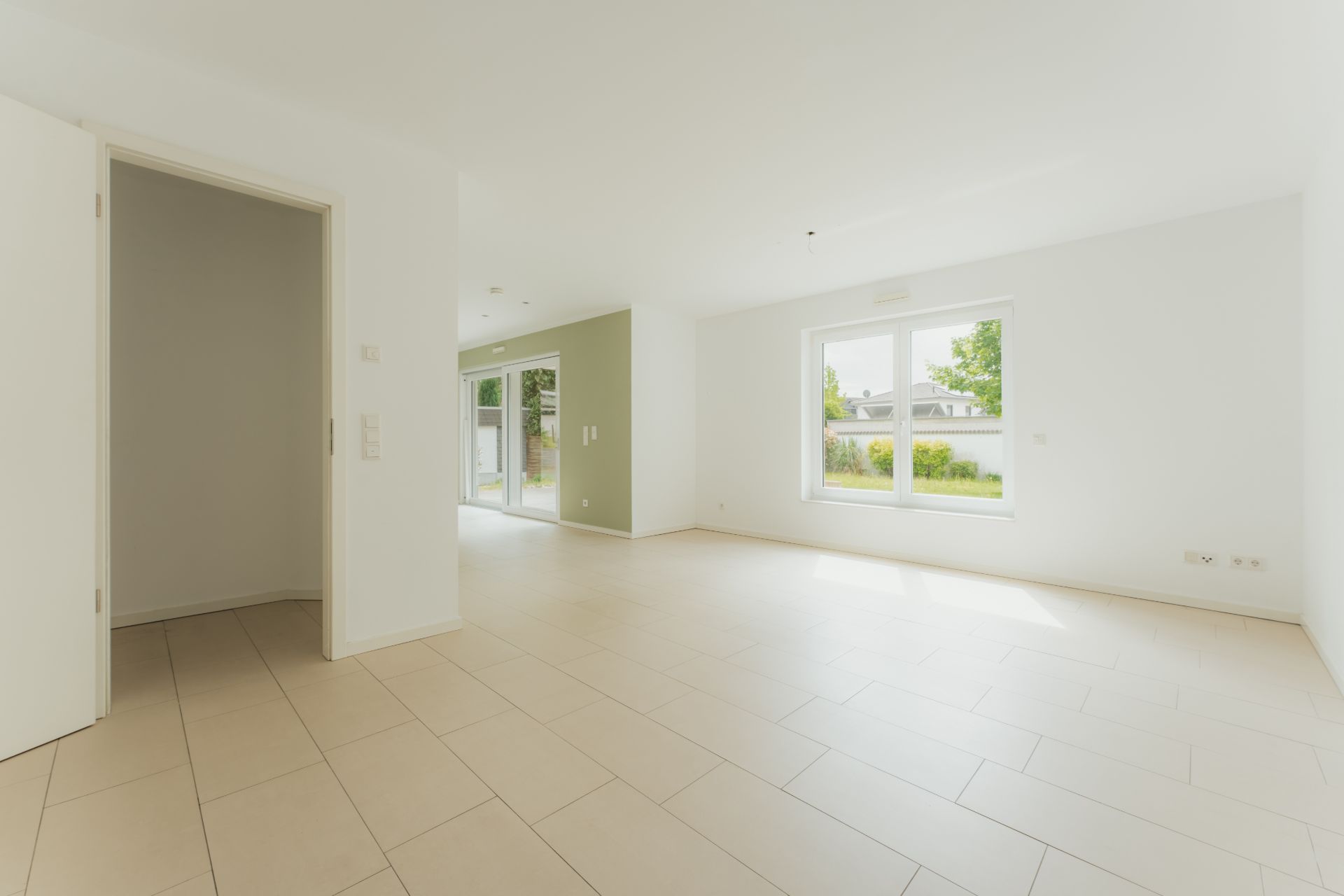 Helles, leeres Wohnzimmer mit großen Fenstern und Fliesenboden.