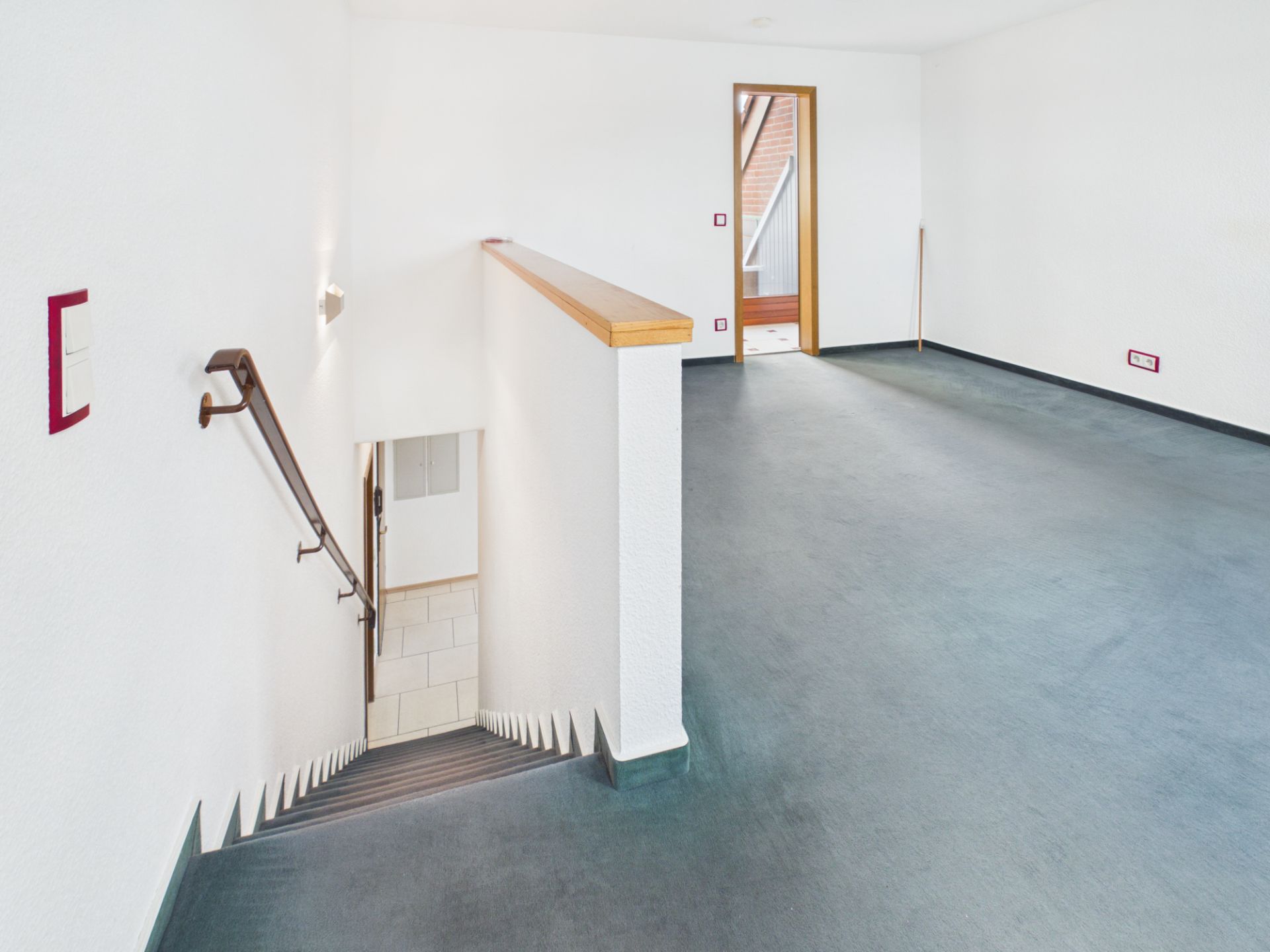 Leerer Raum mit Teppichboden und einer Treppe, die nach unten führt.