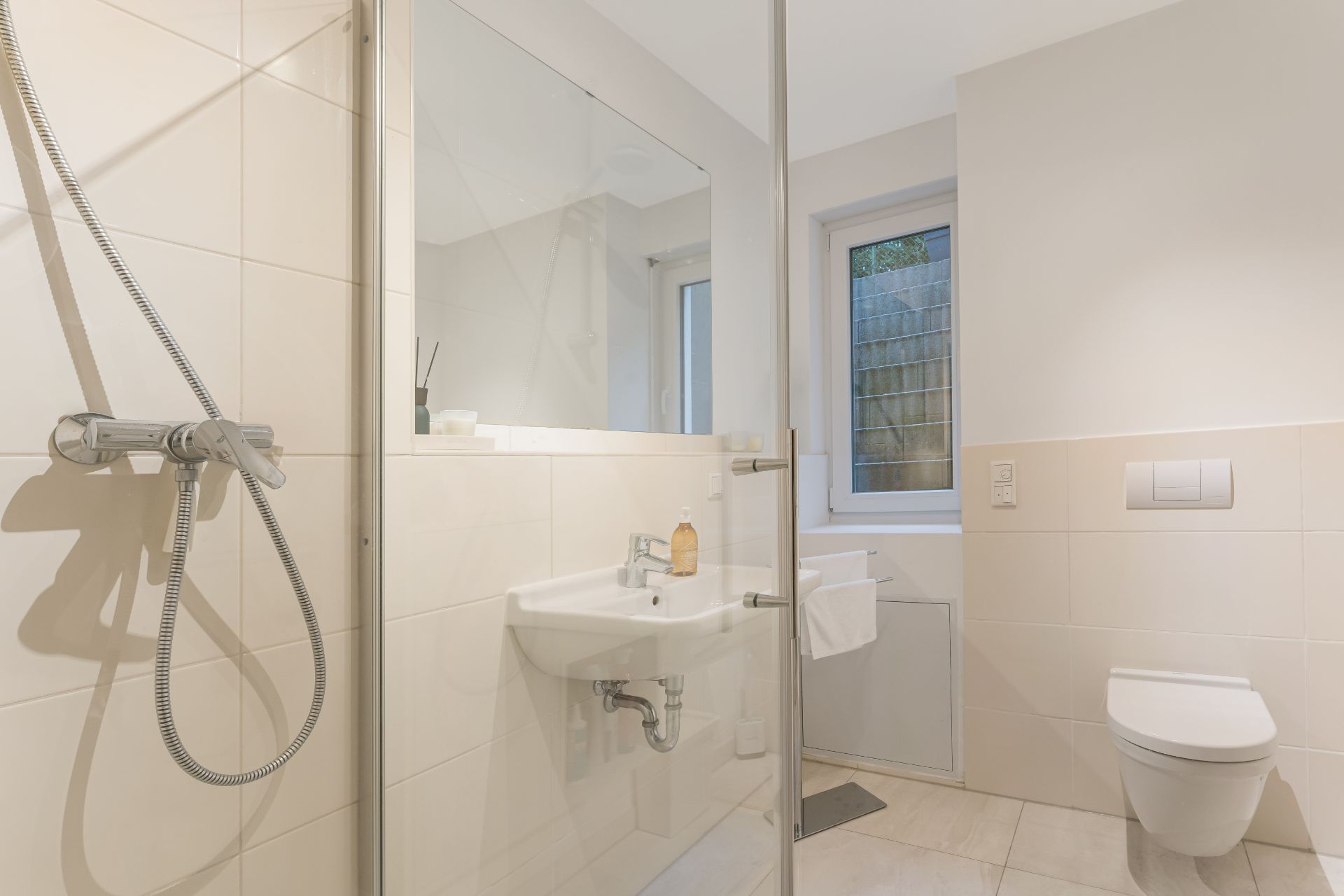 Modernes, helles Badezimmer mit Dusche, Waschbecken, Fenster und wandhängender Toilette.